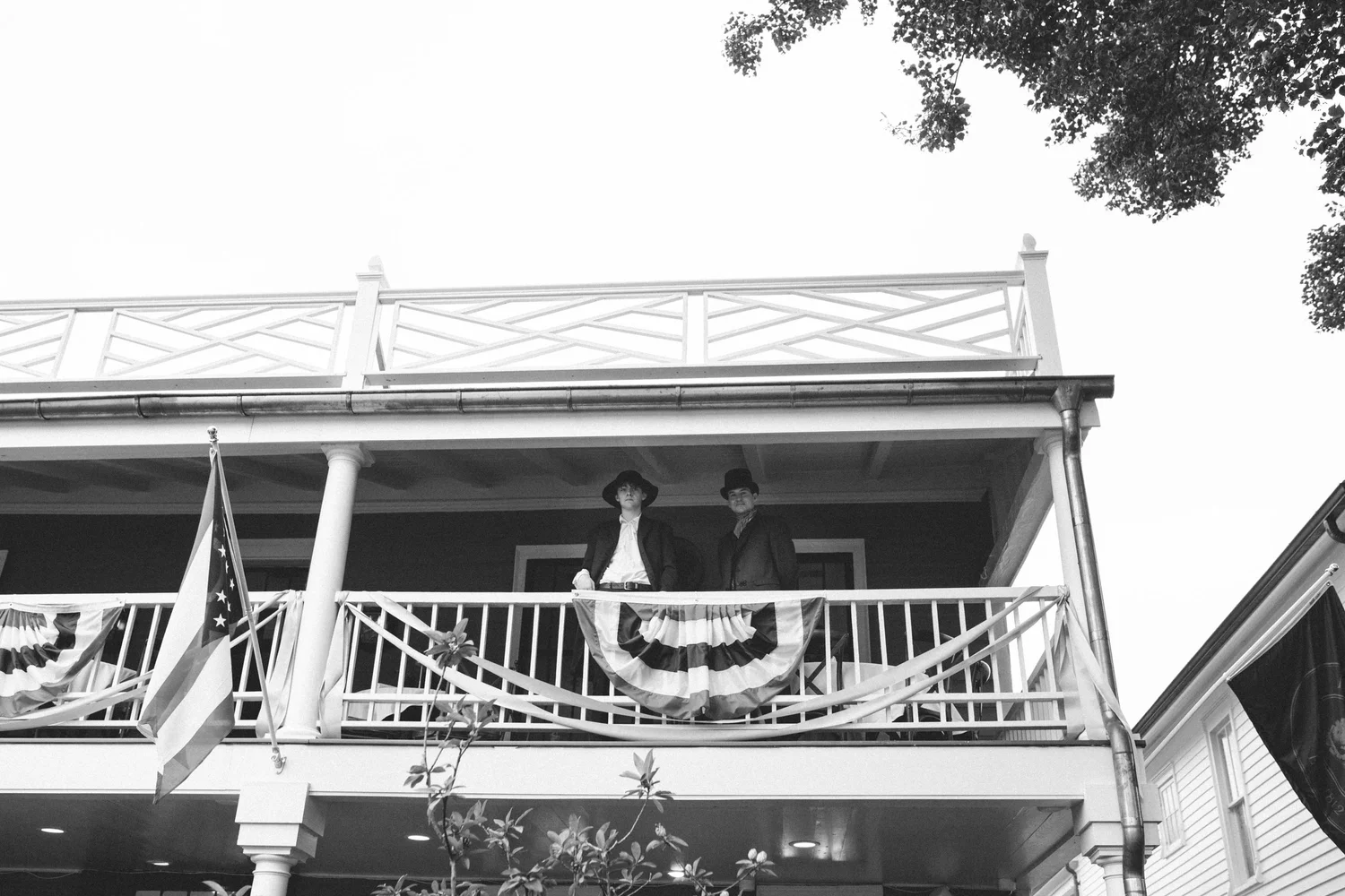 A black-and-white view of costumed participants on the upper porch.