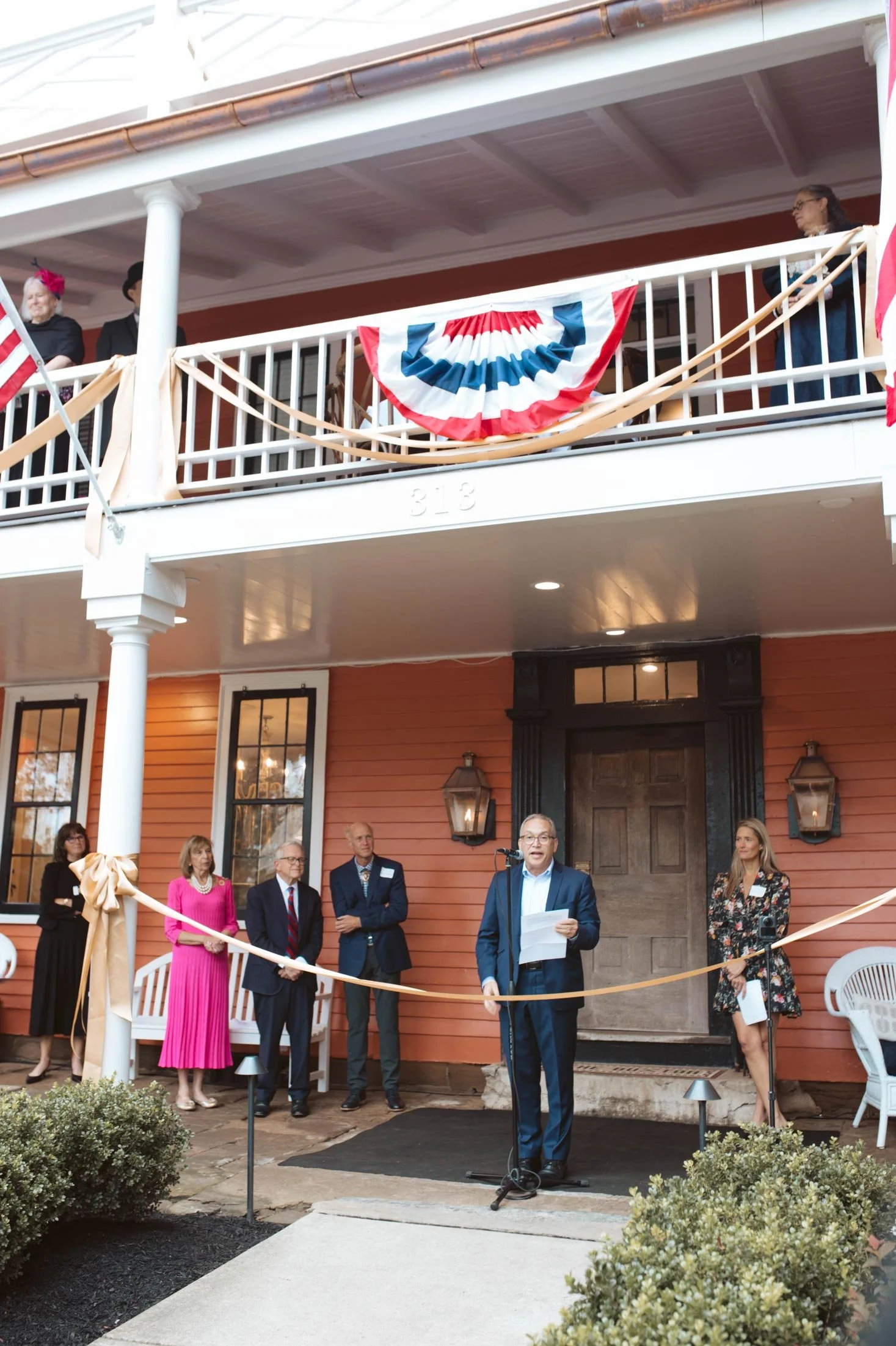 A speaker giving remarks in front of the inn before the ribbon cutting.