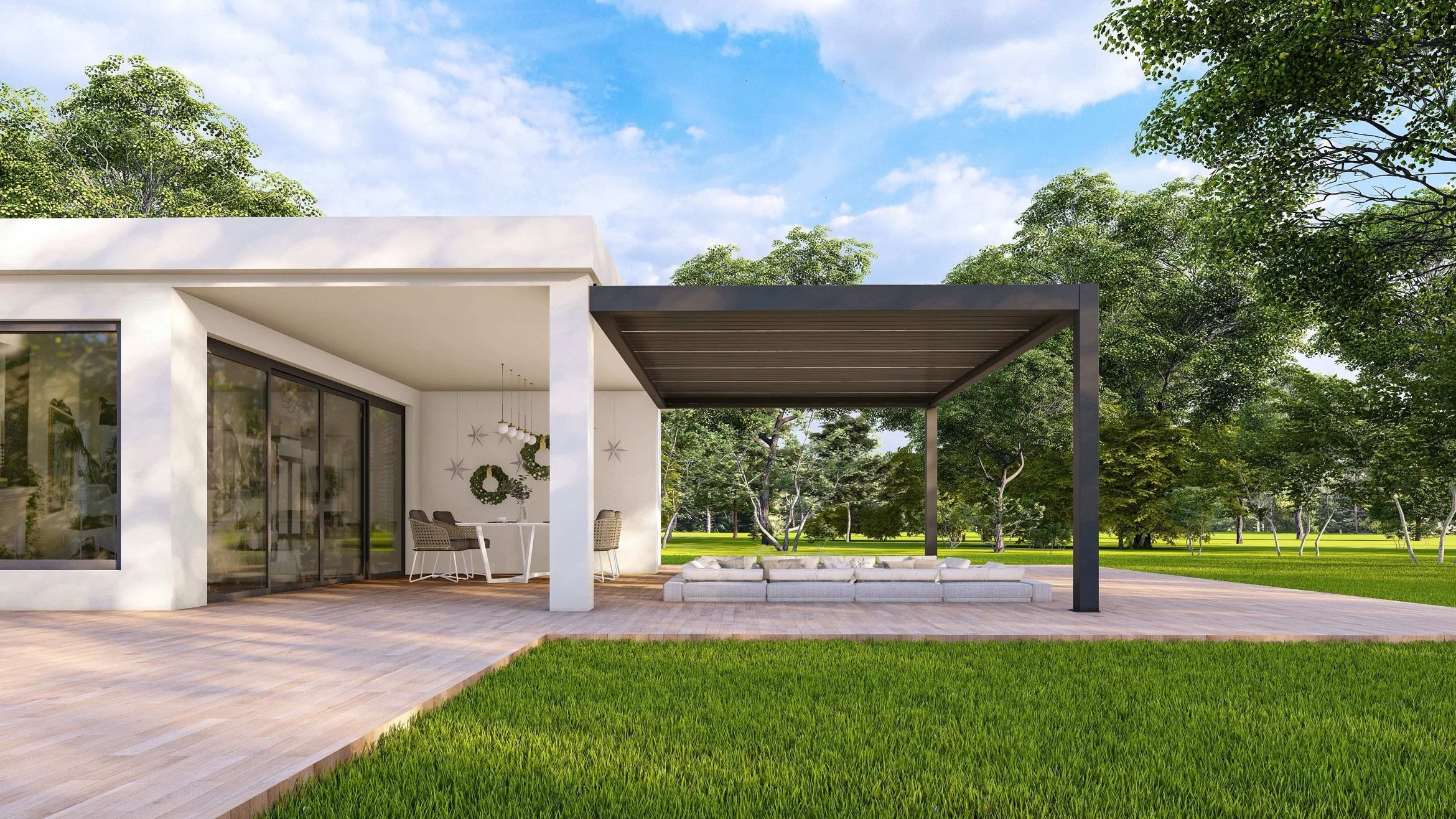 Modern house with large glass sliding doors and a covered outdoor patio area with seating, set in a lush green landscape with trees and grass under a blue sky.