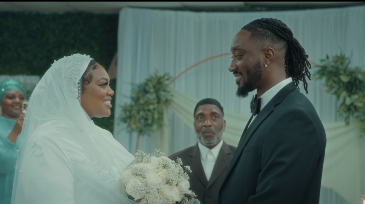 A bride and groom look at each other during their wedding ceremony, with an officiant and bridesmaid visible in the background.