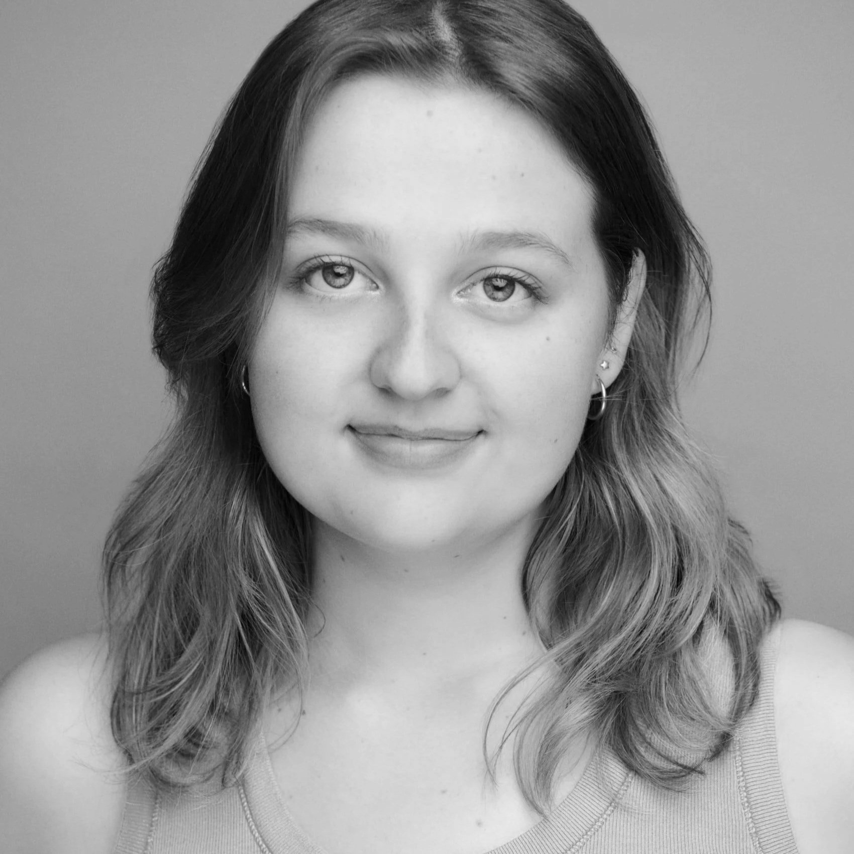 Black and white portrait of a young woman with wavy hair, wearing and a tank top, smiling slightly.