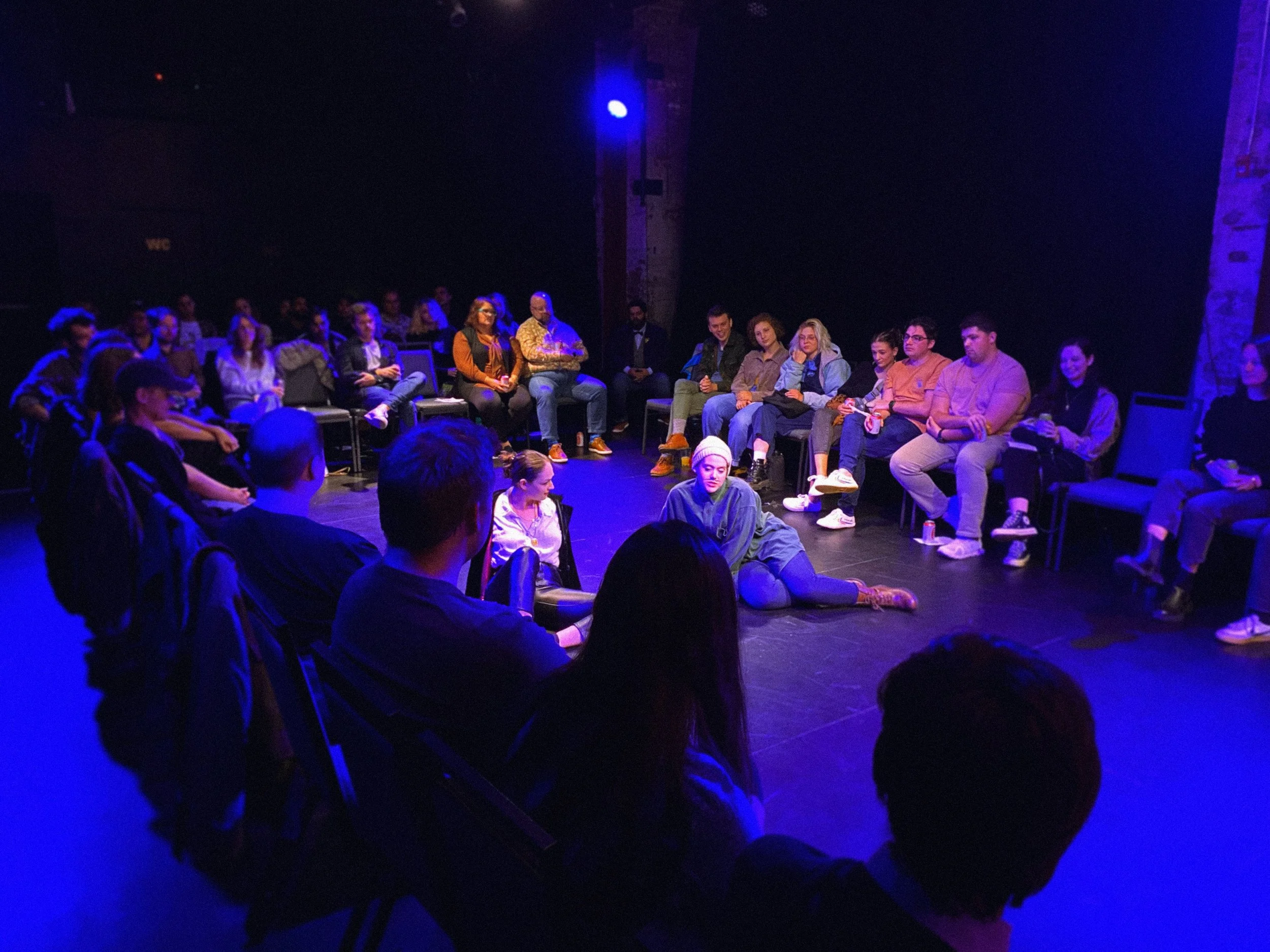 Audience members sitting in chairs in a dark venue with blue lighting.