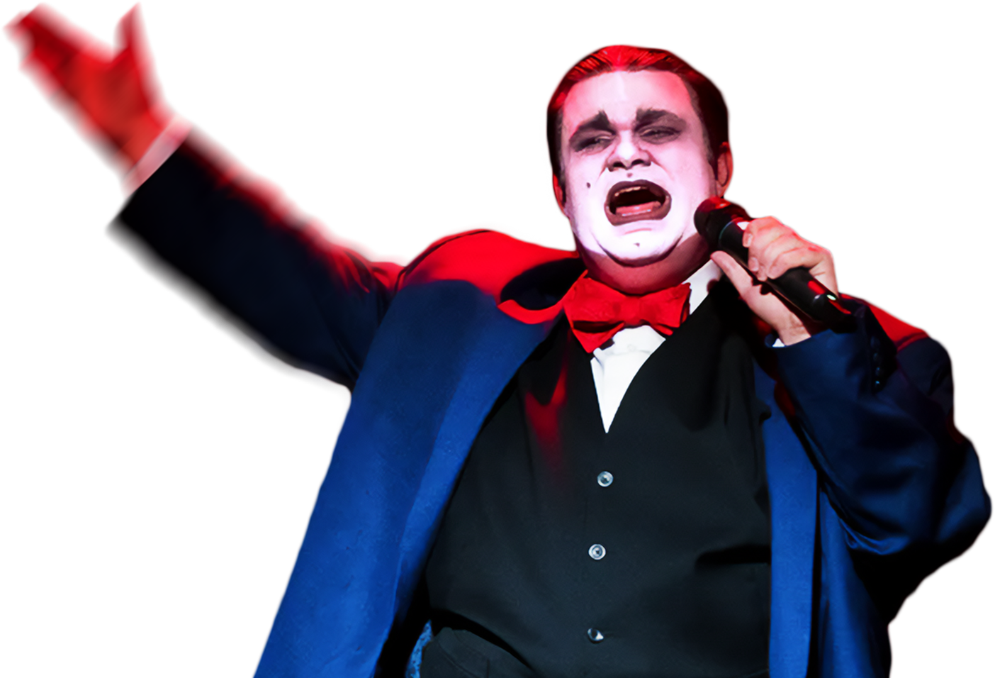 A performer dressed with white face paint and red accents, wearing a dark suit, red bow tie, and holding a microphone while singing passionately on stage.
