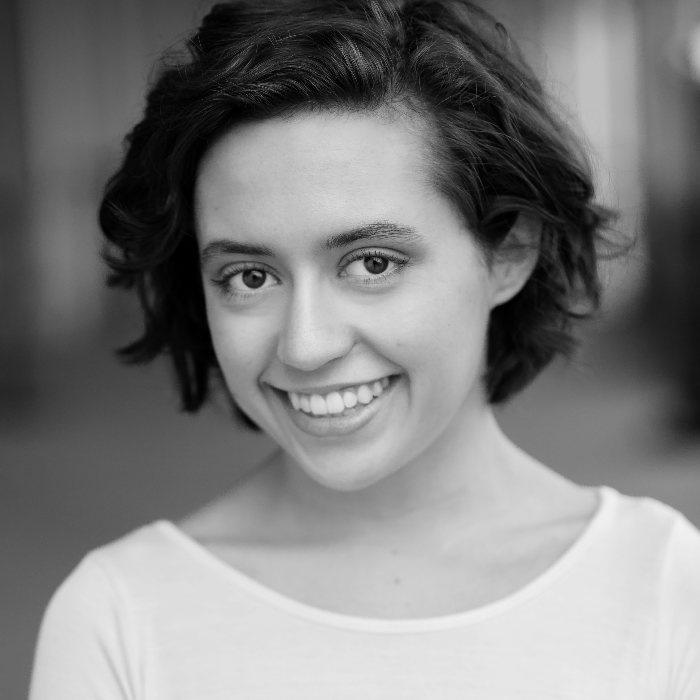 Close-up black-and-white portrait of a woman's face with curly hair, smiling and showing her teeth.