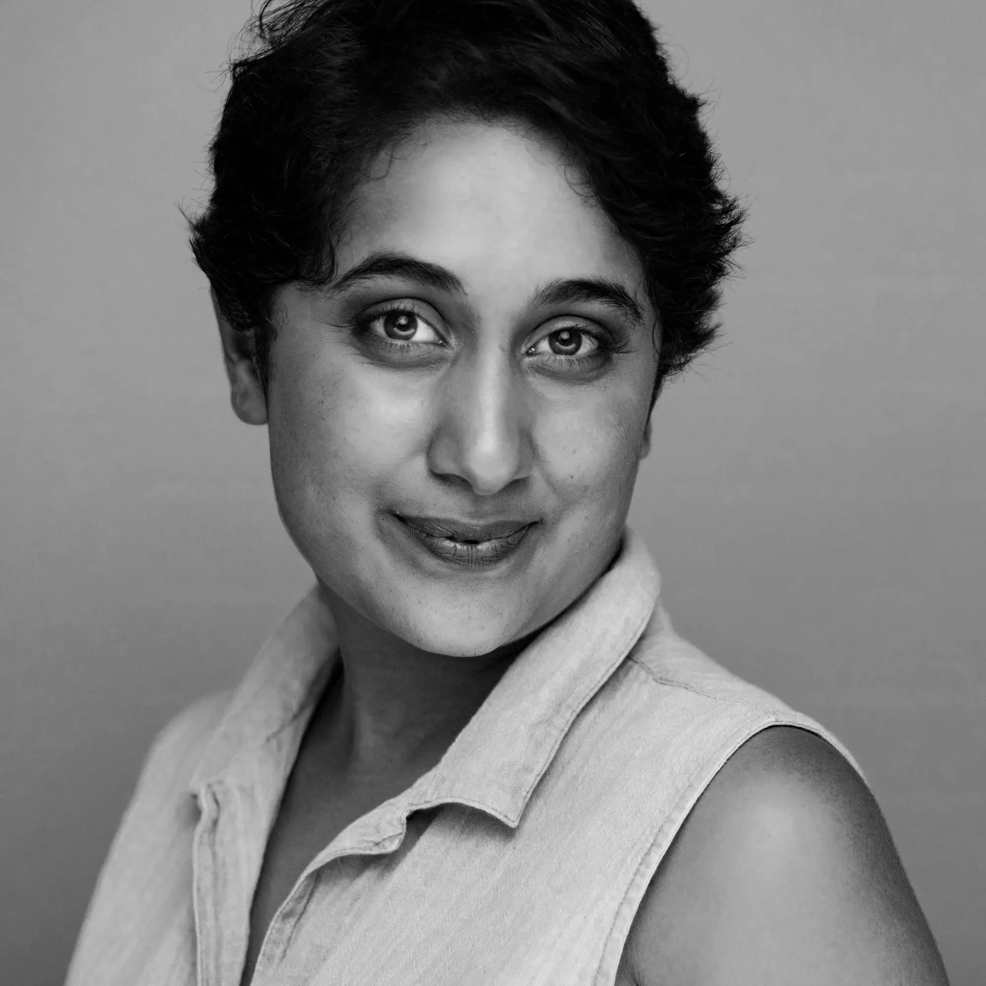 Close-up of a woman's face with short curly hair, smiling slightly, wearing a collared shirt, in black and white.