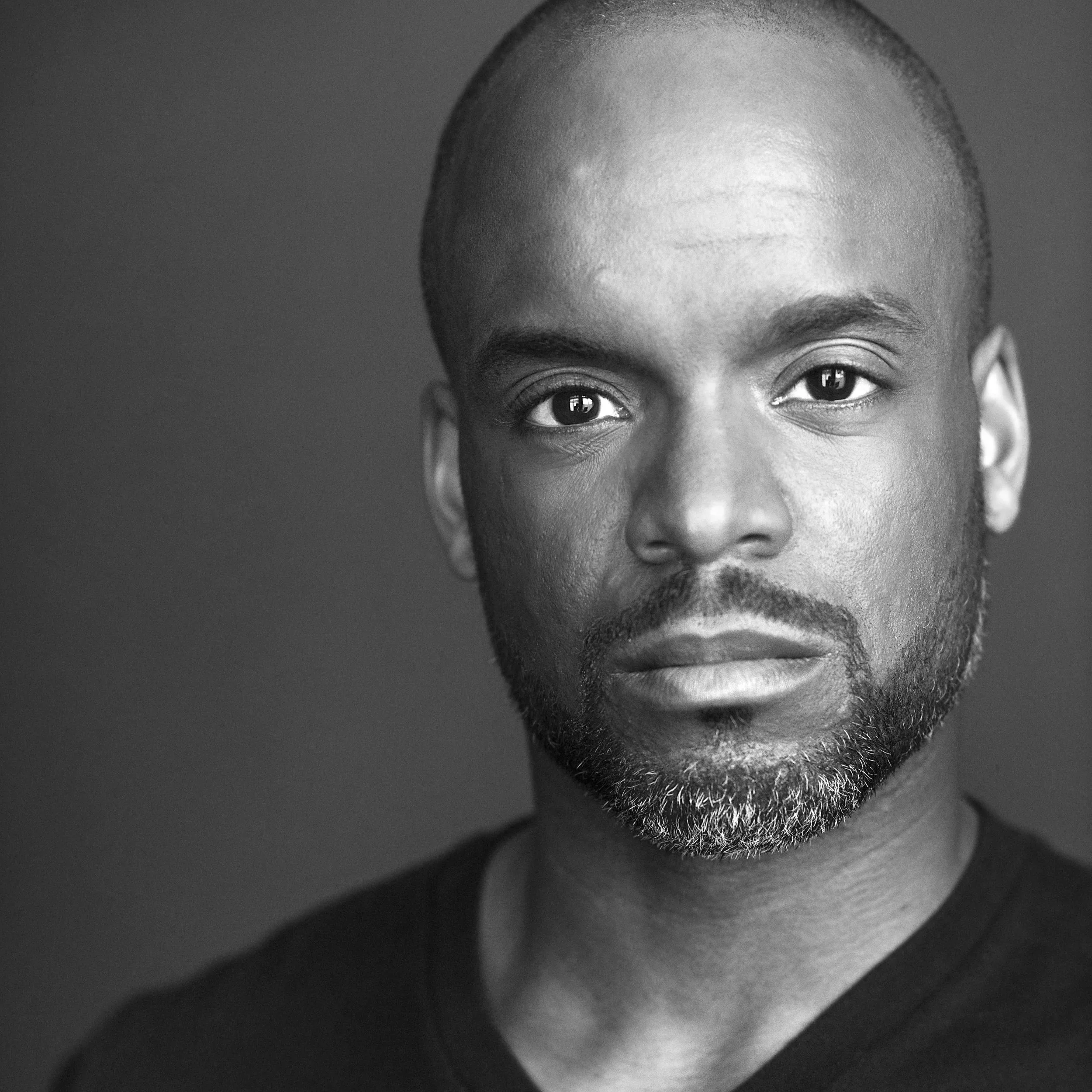 Close-up black and white photo of a with a short beard and a serious expression.