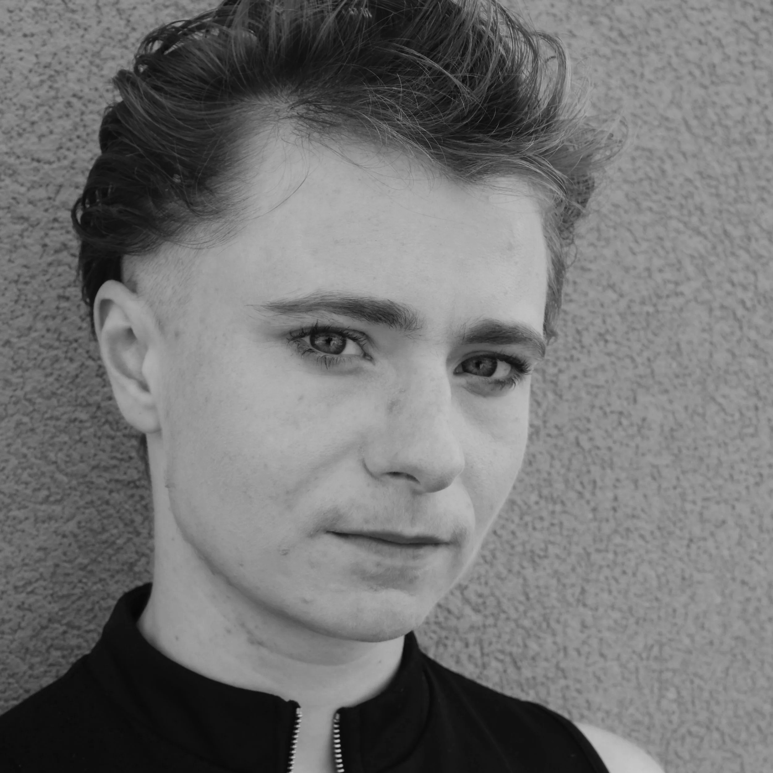 Close-up of a person's head showing their short hair and part of their face, on a textured background.