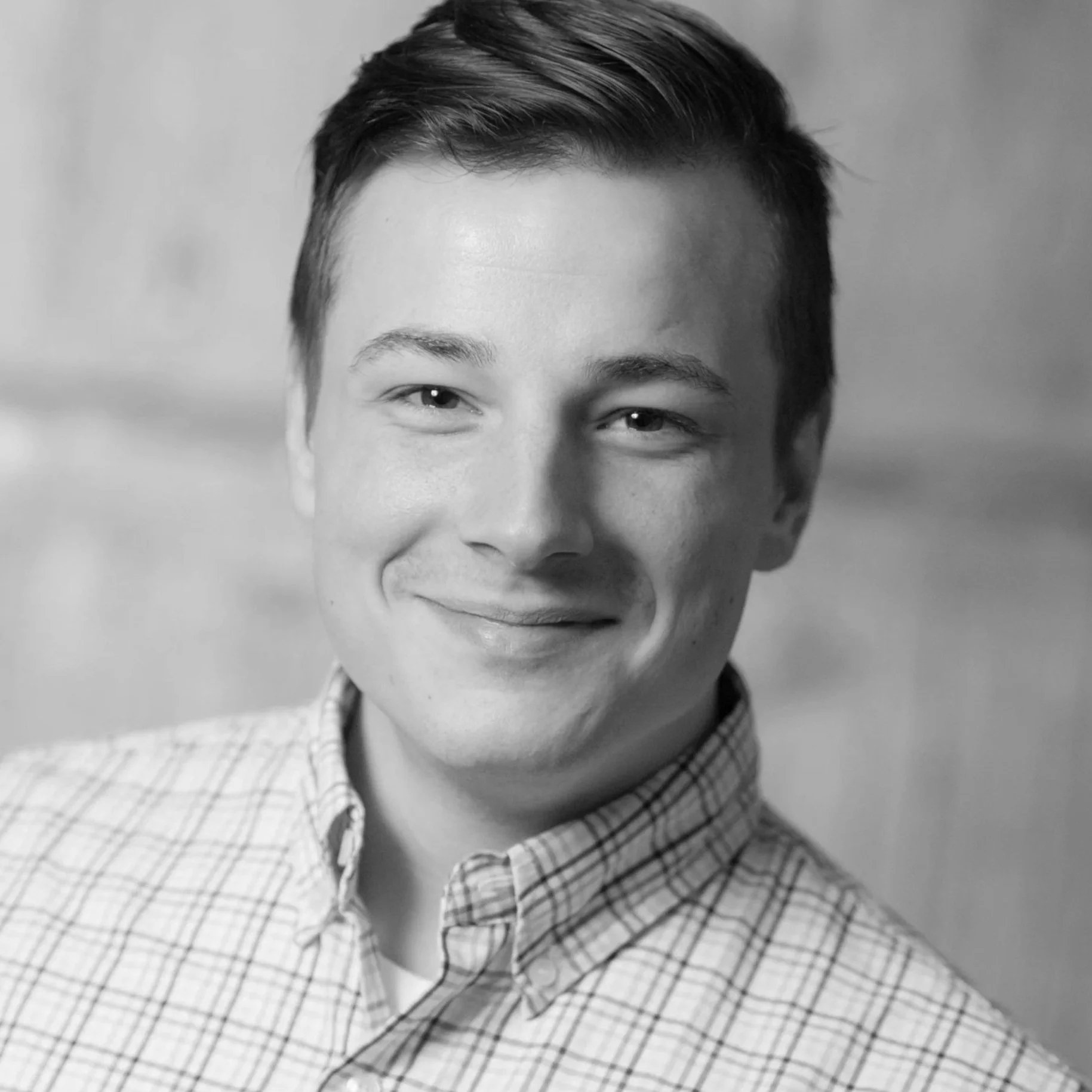 Black and white photo of a smiling person with short dark hair, wearing a checkered dress shirt.