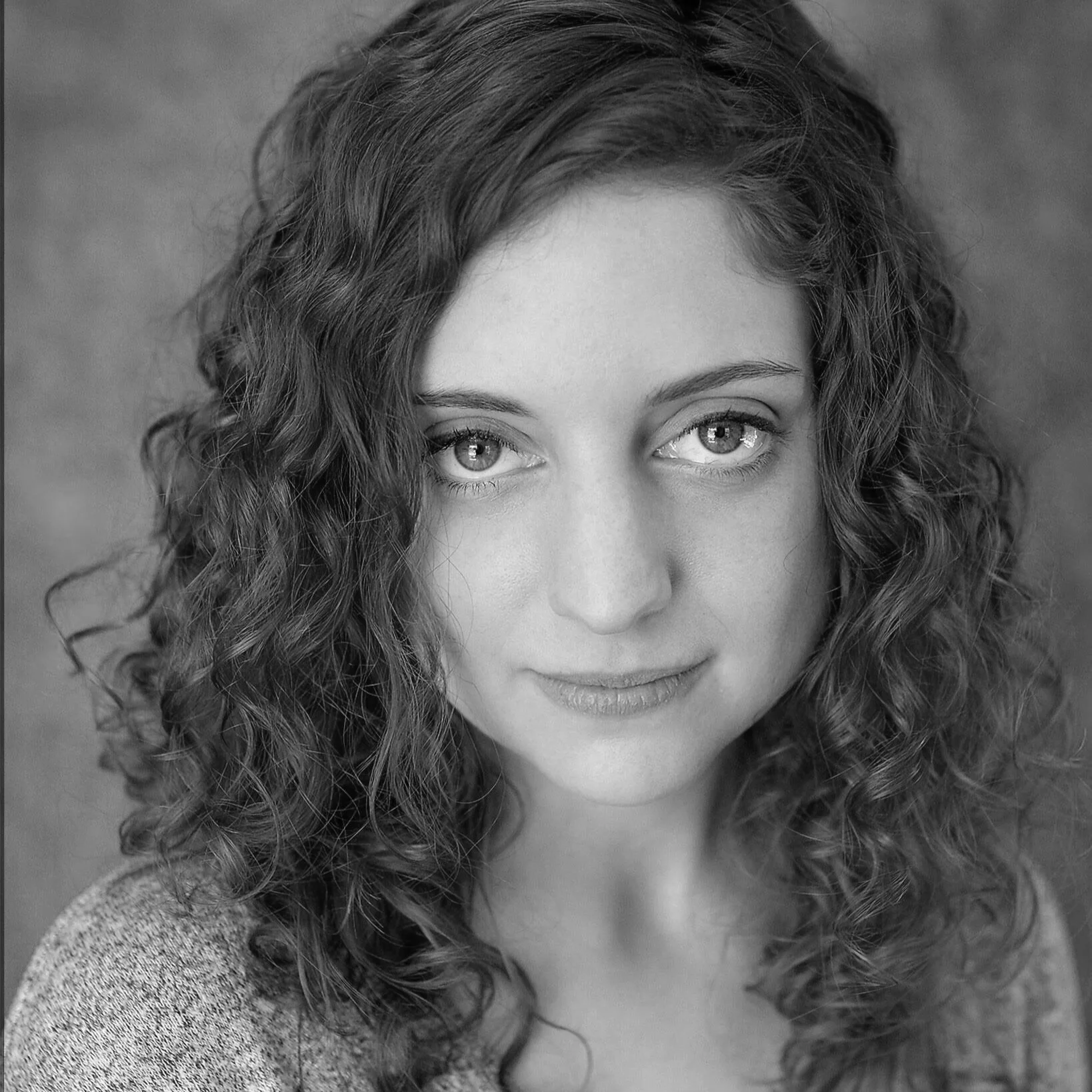 Close-up black and white portrait of a woman with wavy hair, looking at the camera with a slight smile.