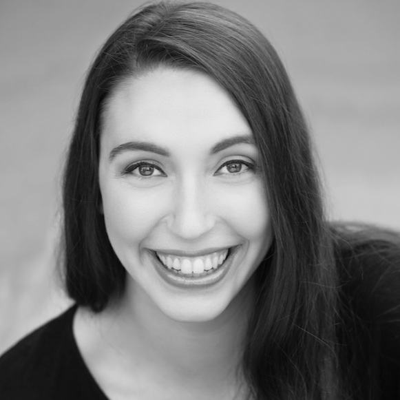 A smiling person with long dark hair looking directly at the camera, with a blurred outdoor background.