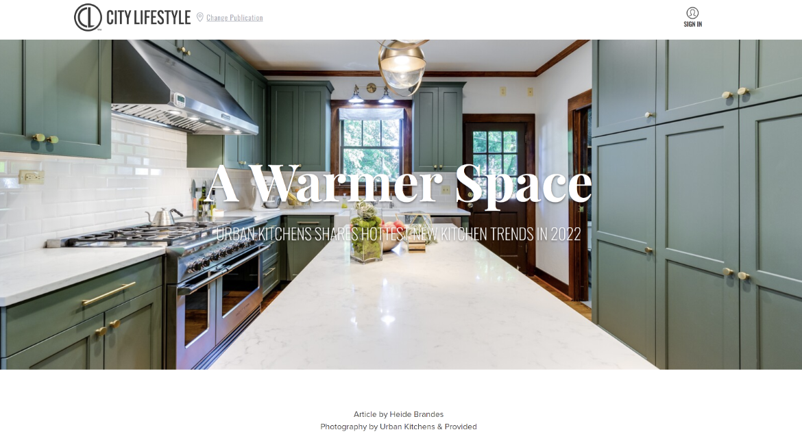 Screenshot of a webpage titled "A Warmer Space" featuring an open kitchen with green cabinets, a white countertop, and a large window letting in natural light.
