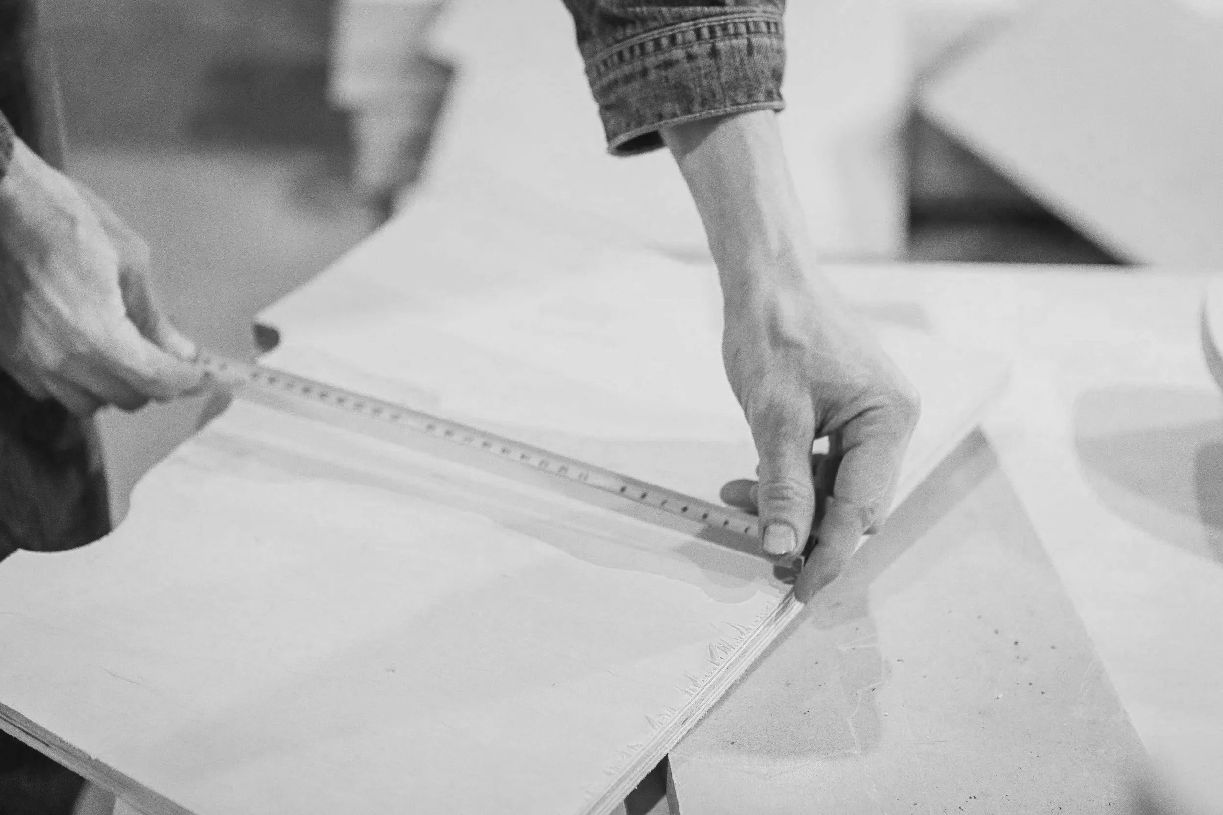 A person's hands are measuring and marking a sheet of paper with a ruler and pencil, likely for a craft or sewing project.