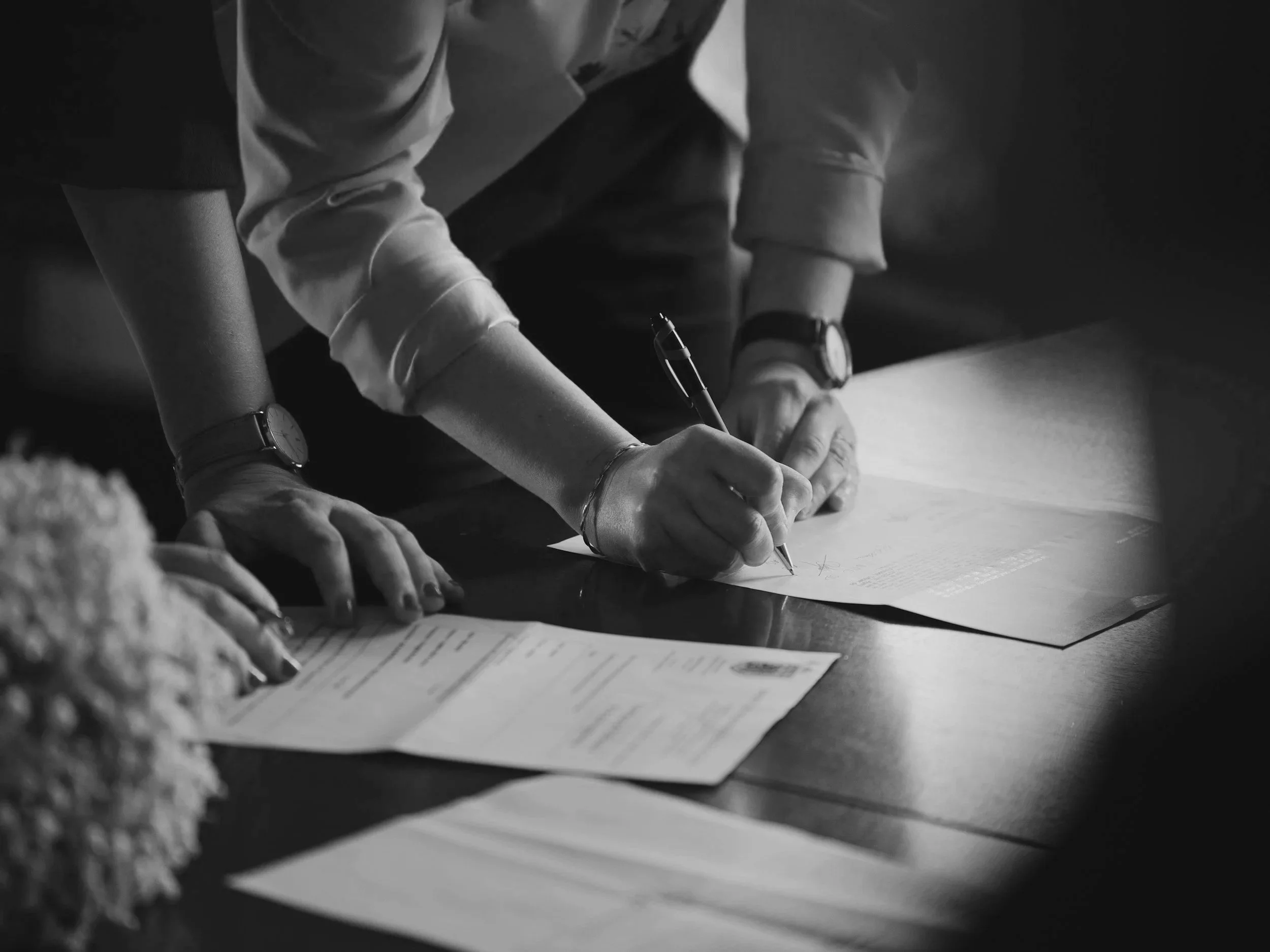 People gathered at a table, writing or taking notes on papers in a black and white photo.