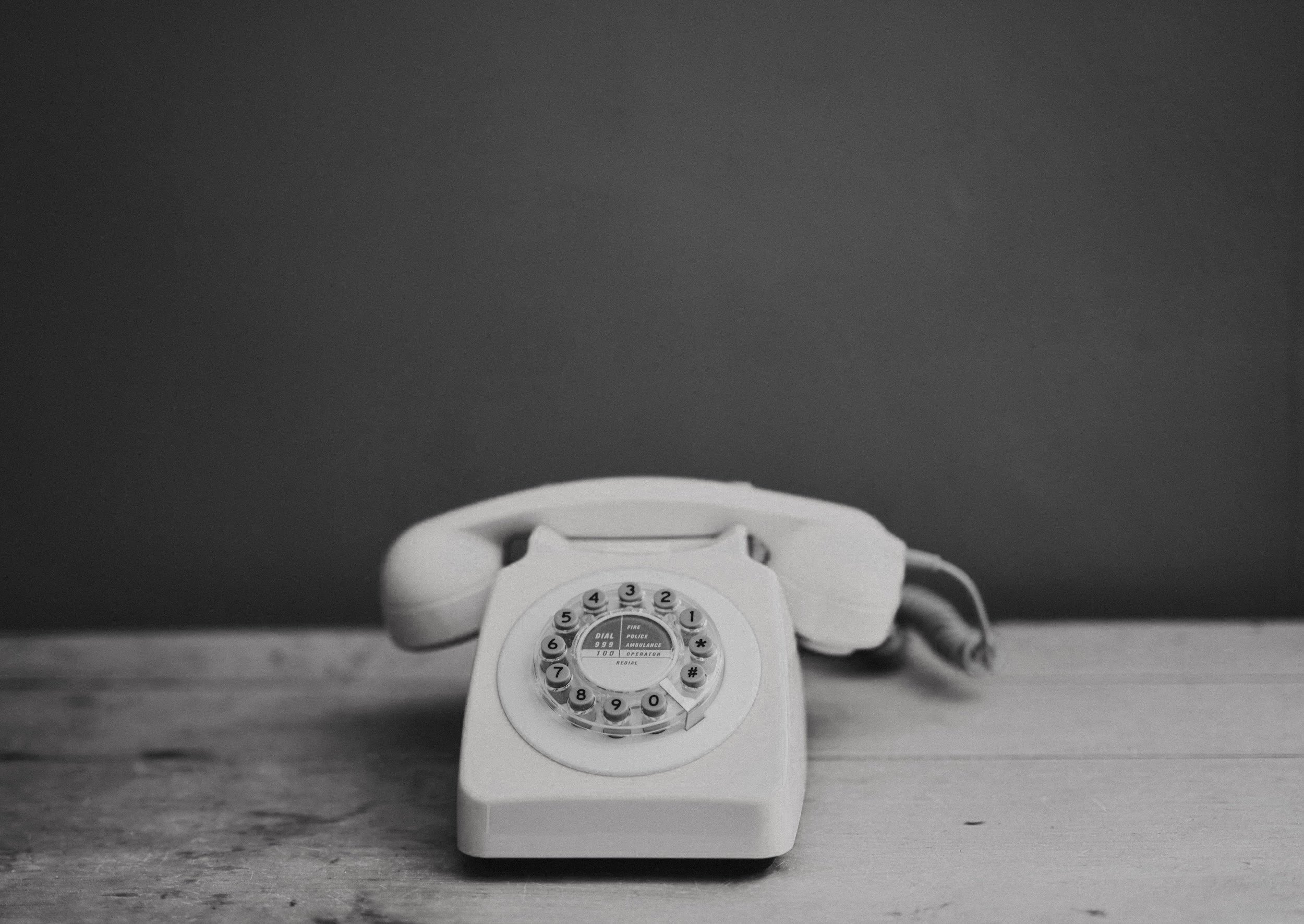 A vintage rotary phone sitting on a wooden surface with a plain dark background.