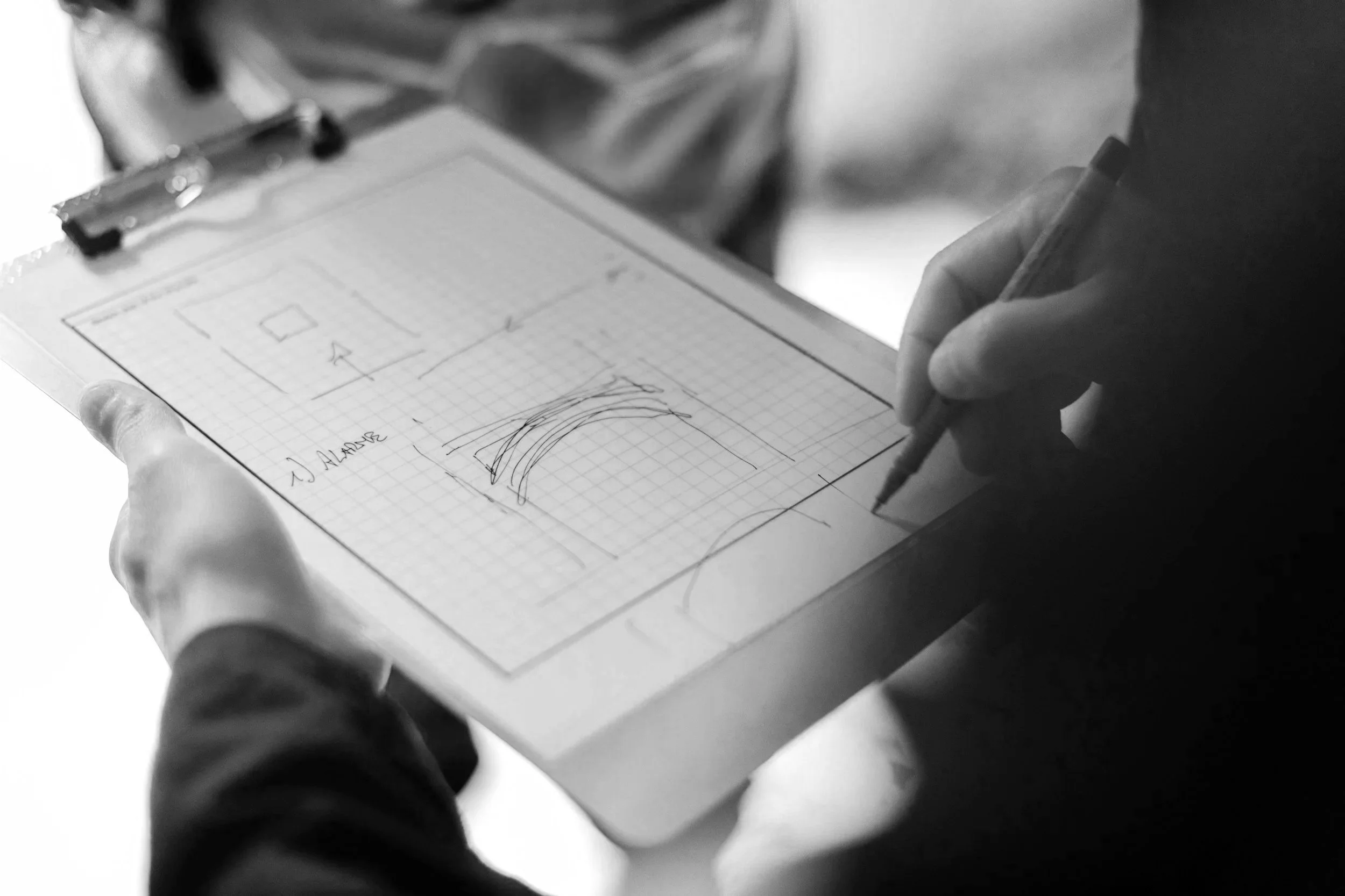 Person holding a clipboard with sketches and notes, taking notes with a pen.