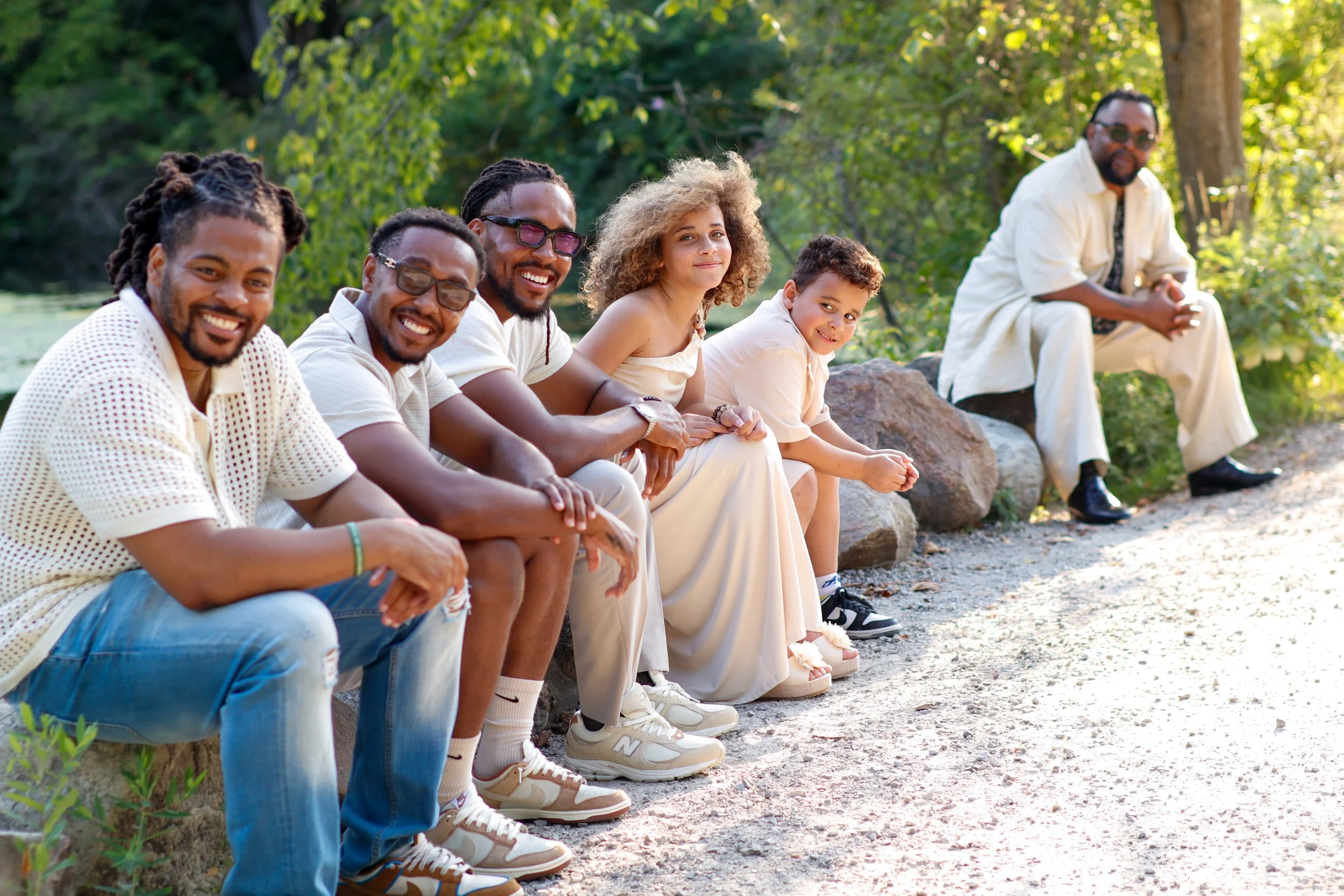 Group of six people sitting outdoors on rocks in a green park, smiling and relaxing.