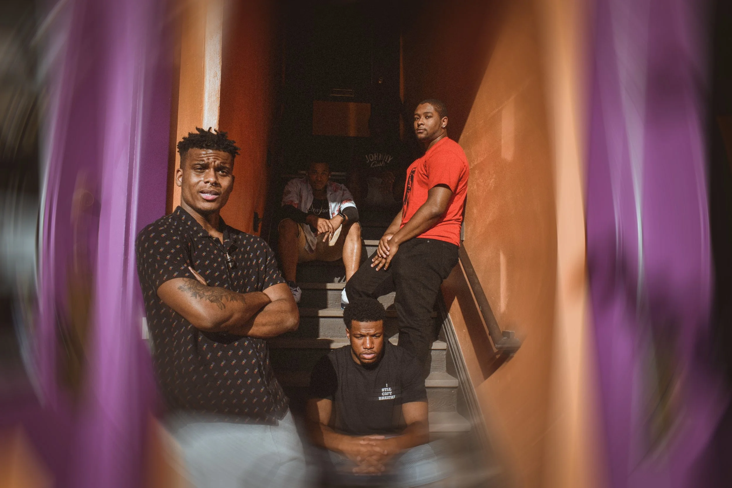 Group of five young men sitting and standing on a staircase, framed by a colorful tunnel effect.