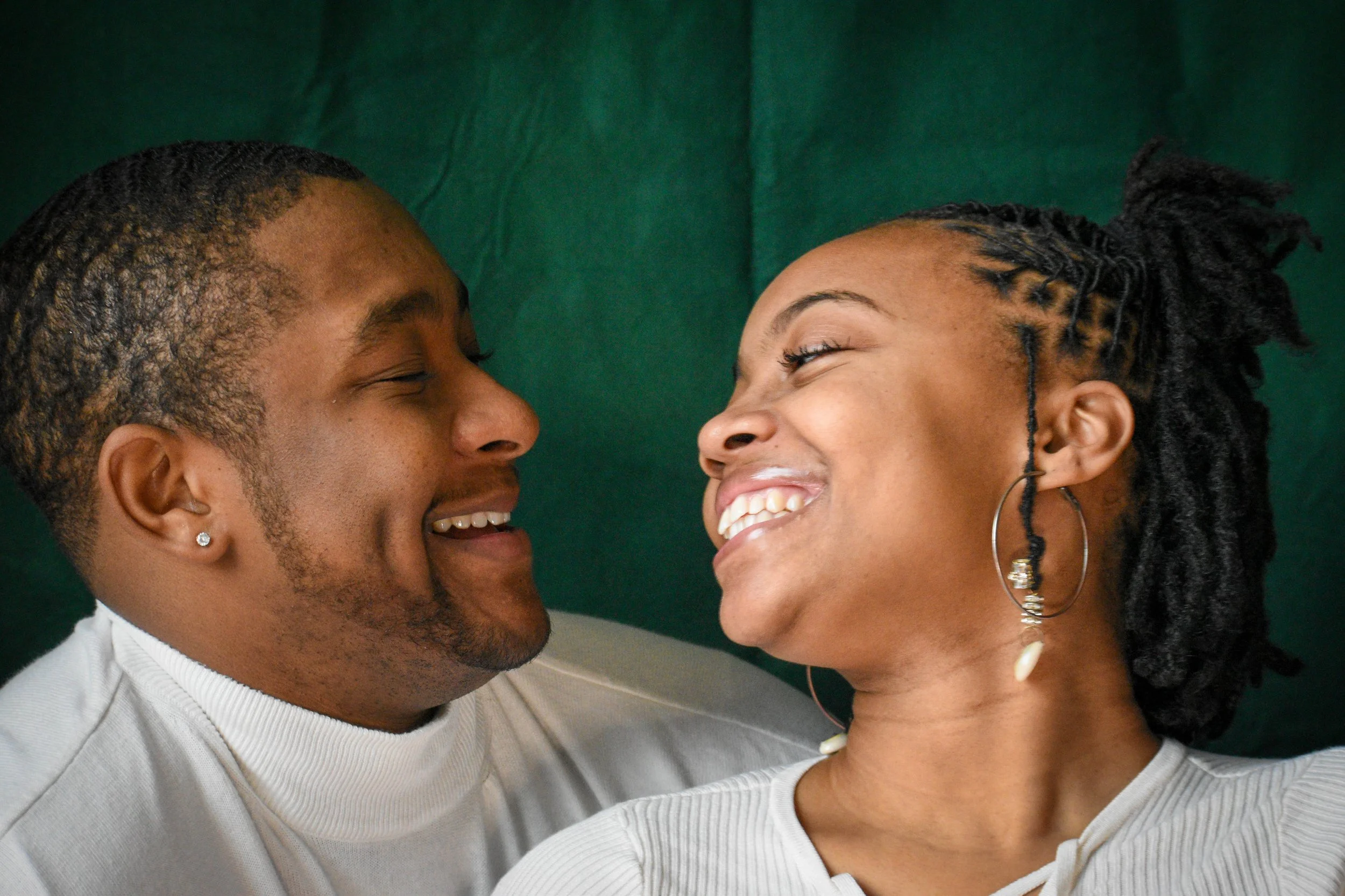 Two people, a man and a woman, face to face smiling, close together, with a green background.