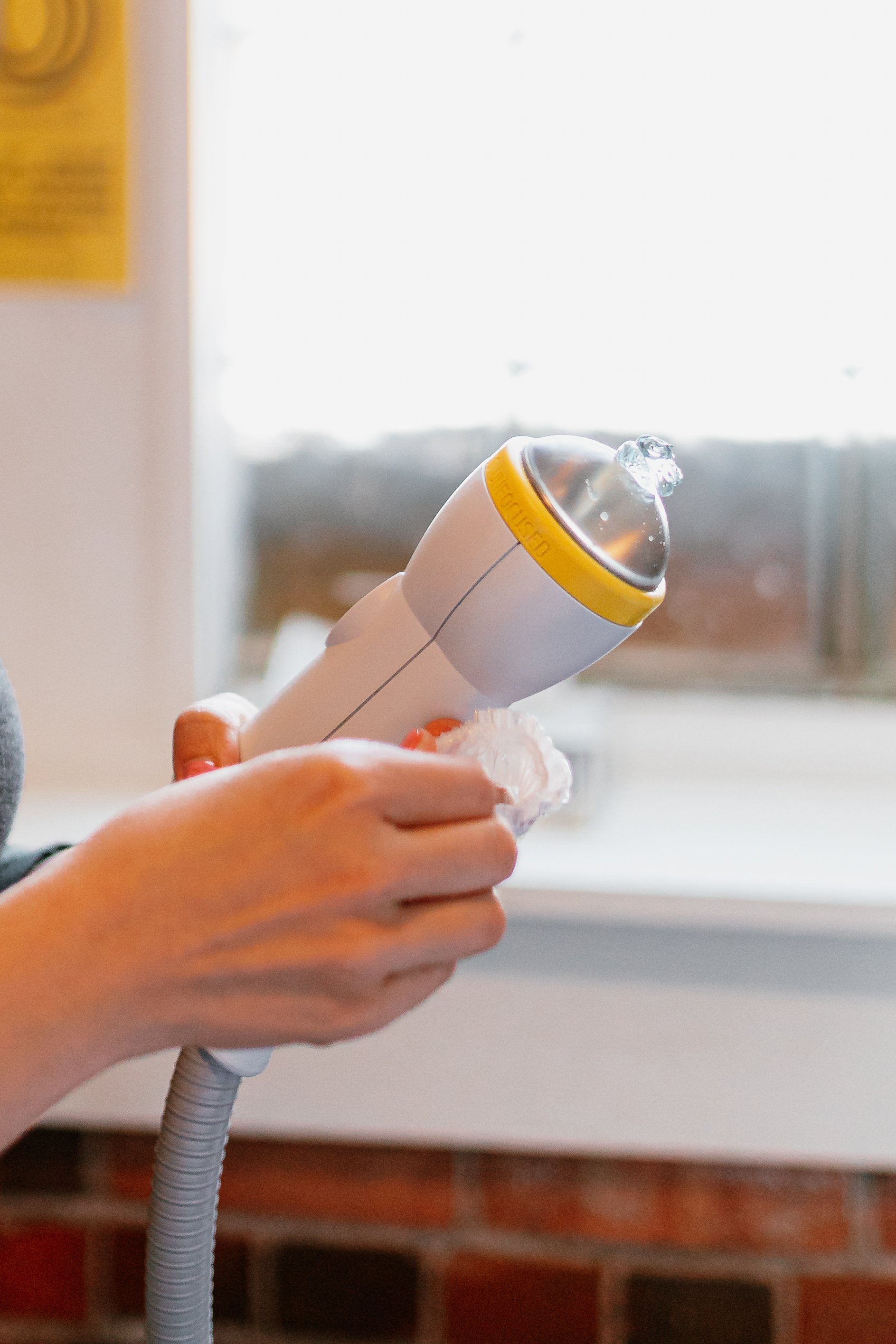 Person holding a handheld device with a clear water droplet on top, against a bright window background.