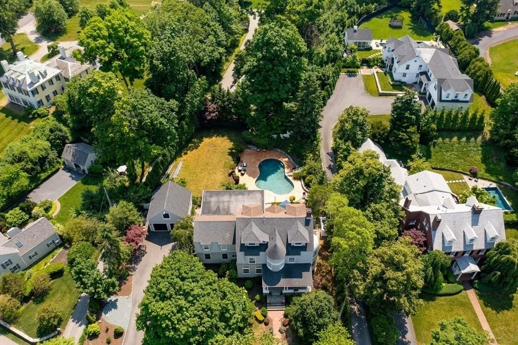 Aerial view of a residential neighborhood with large houses, trees, and a backyard with a swimming pool.