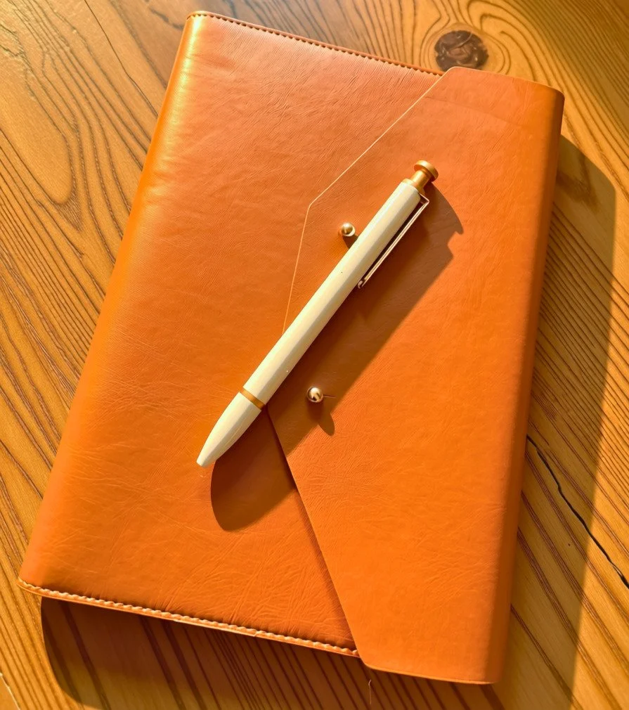 Closed notebook and pen on a desk in warm light