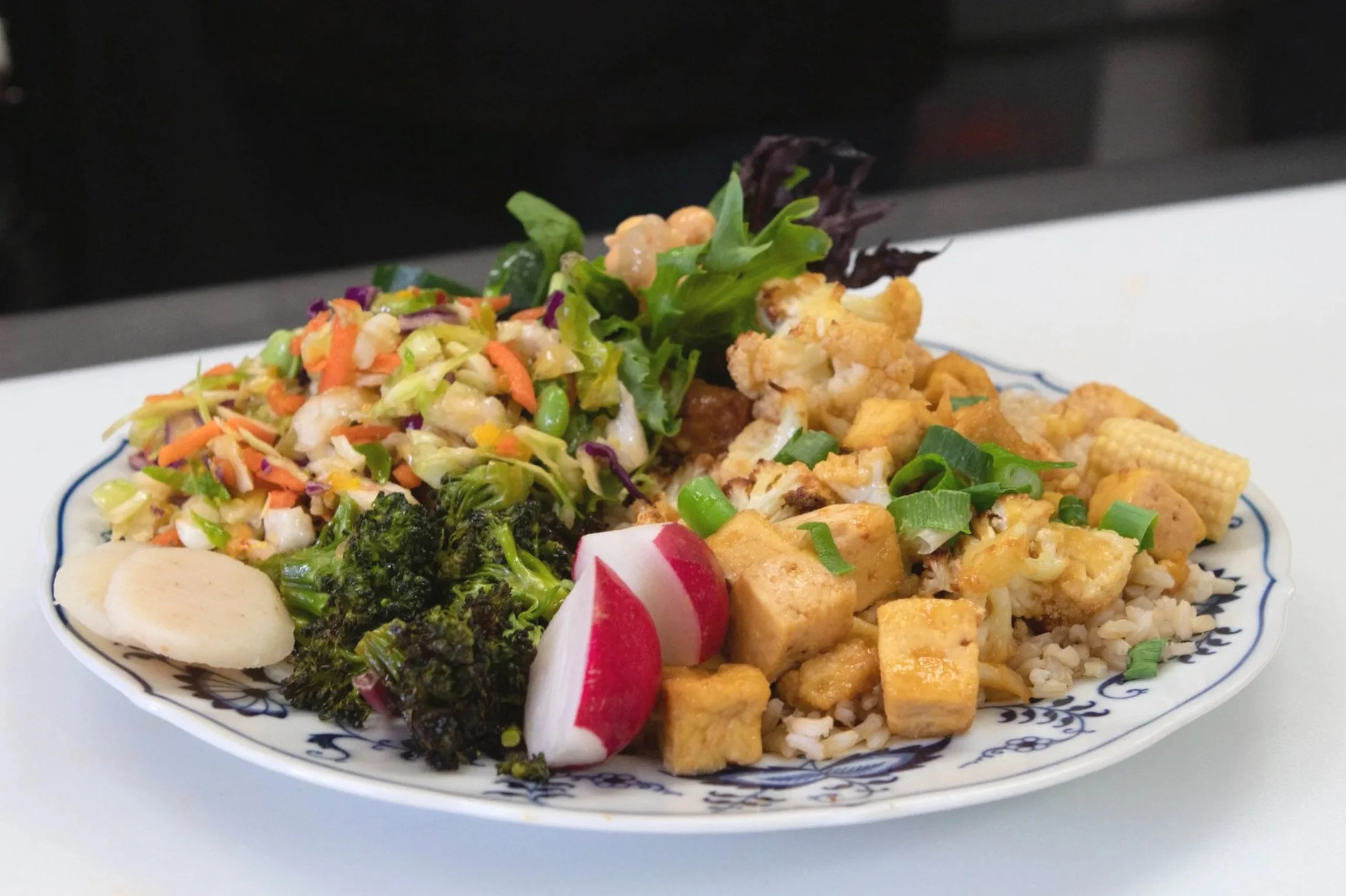 A plate of mixed Asian cuisine including noodles, fried tofu, vegetables, and salad garnished with radish slices.