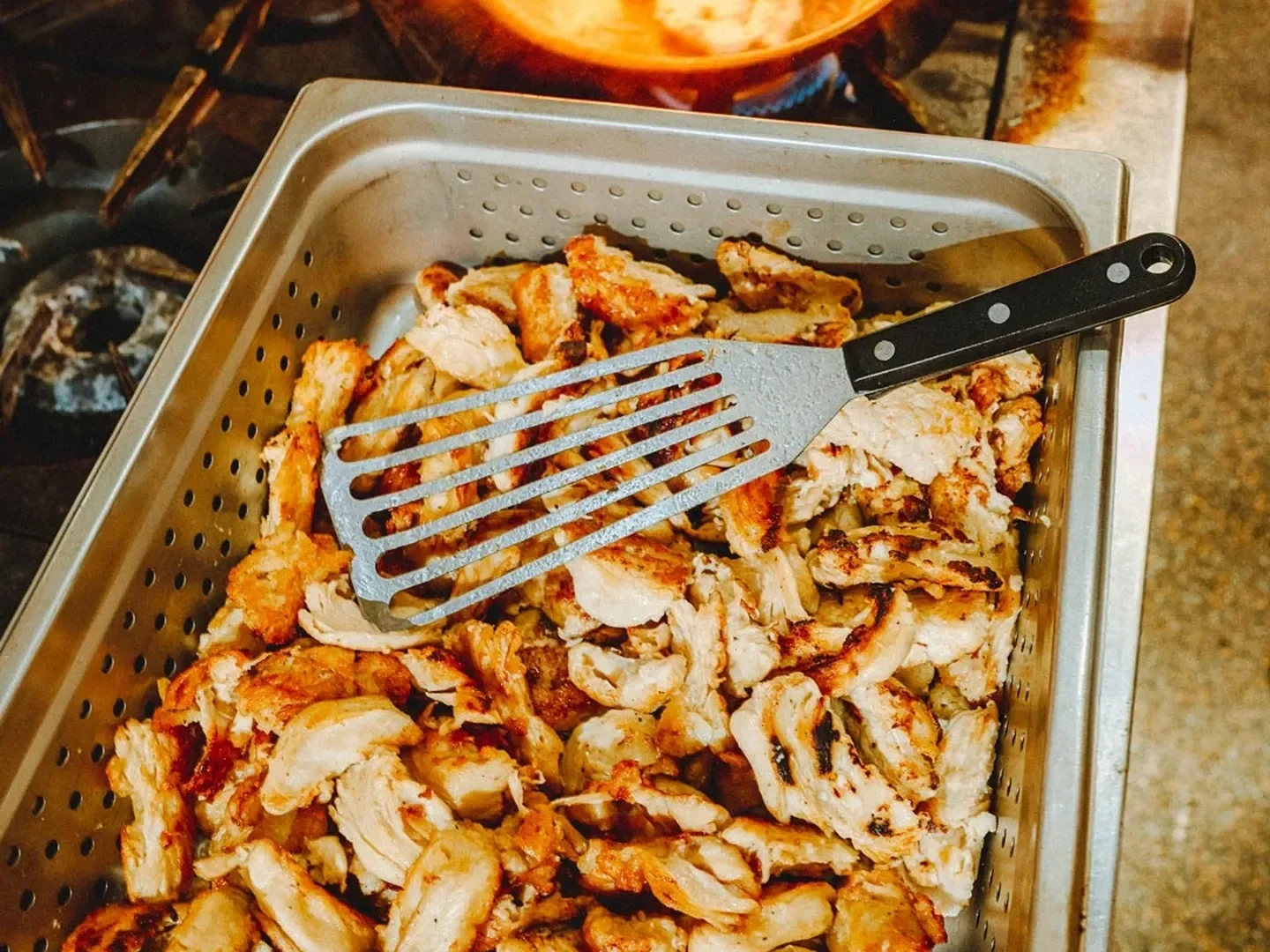 Cooked shredded plant-based chicken in a metal colander with a slotted spatula on top.