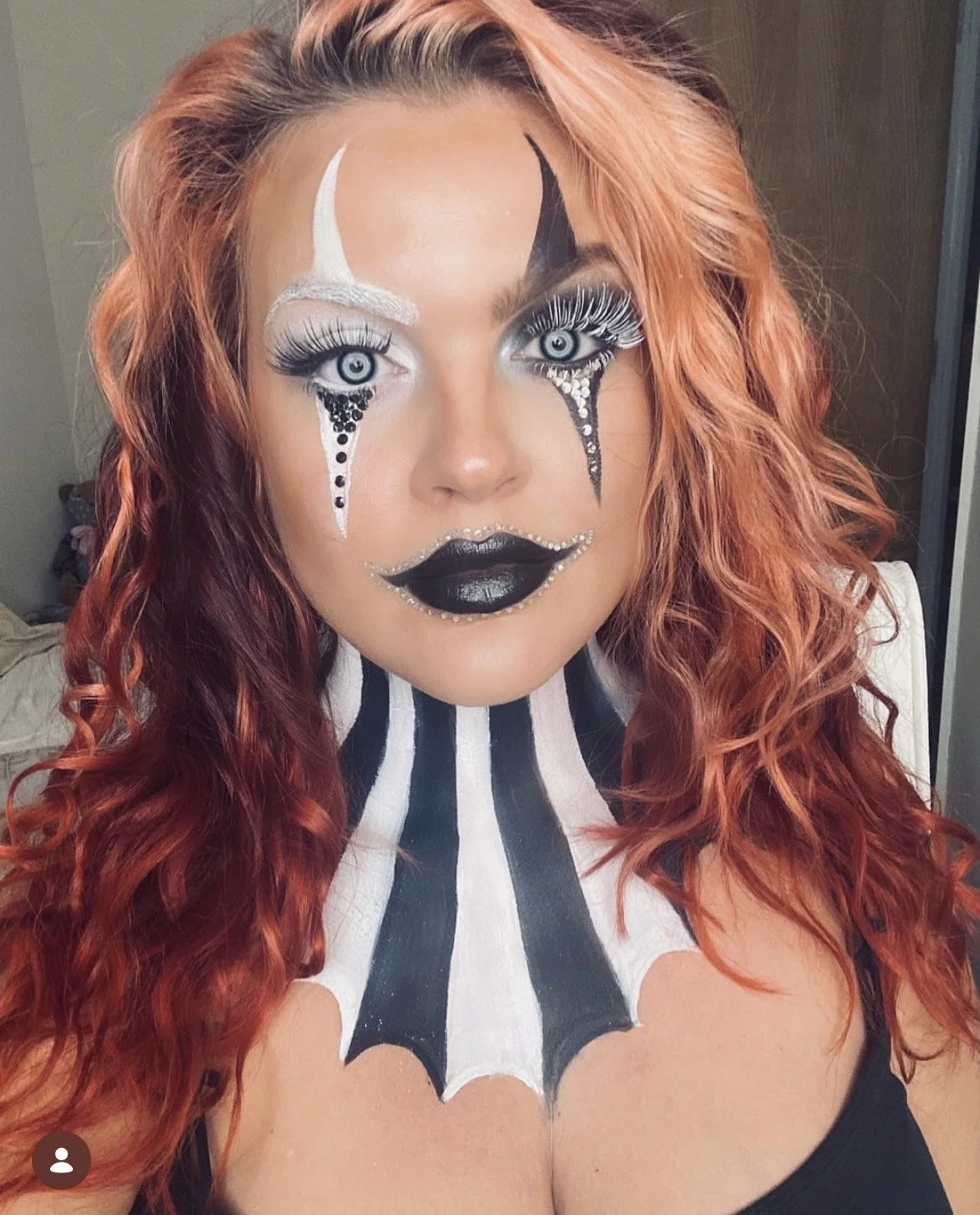 A woman with elaborate black and white clown-inspired makeup and long, curly, reddish-orange hair.
