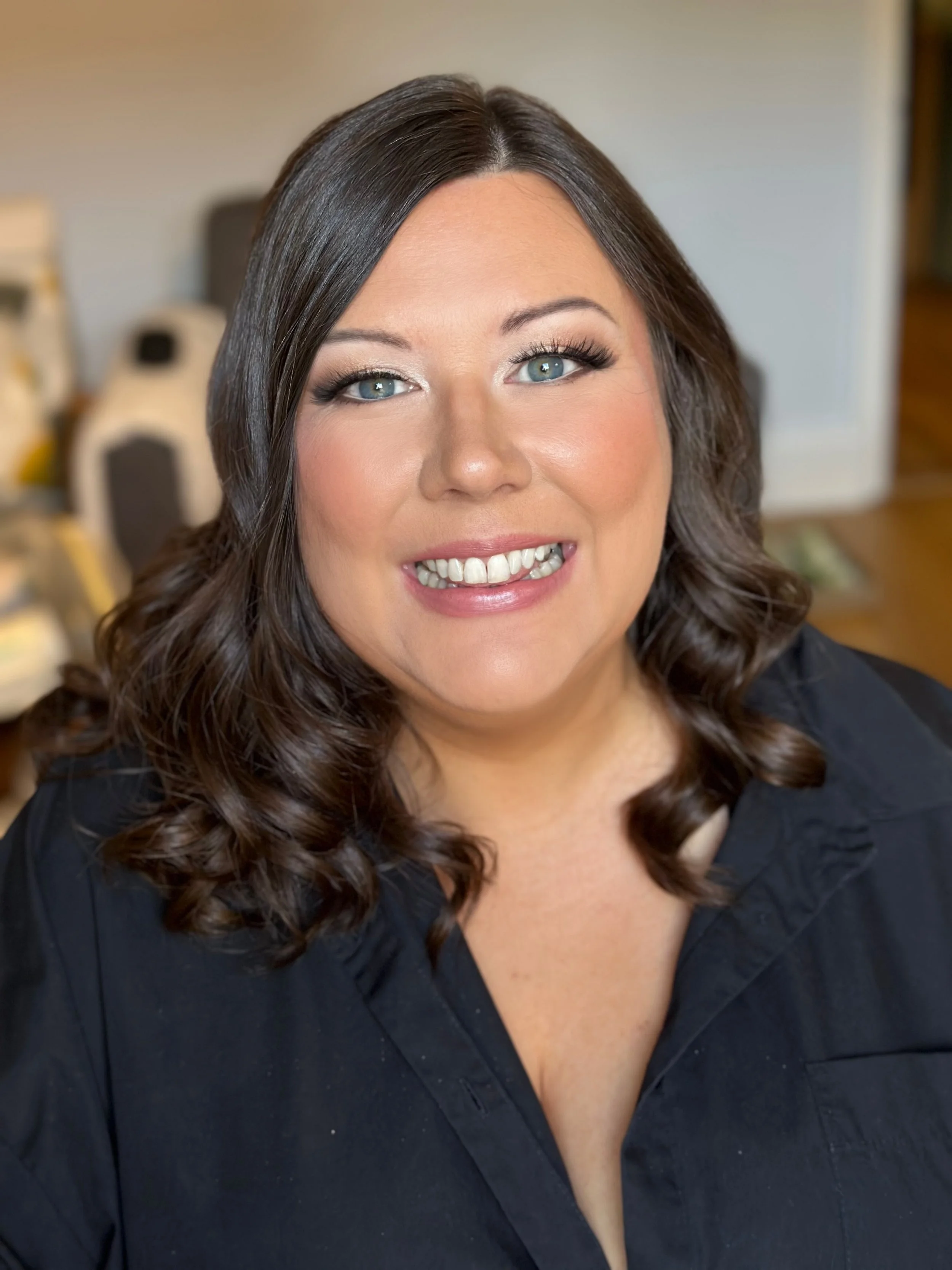 A woman with dark brown, curly hair, blue eyes, and a bright smile wearing a black shirt.