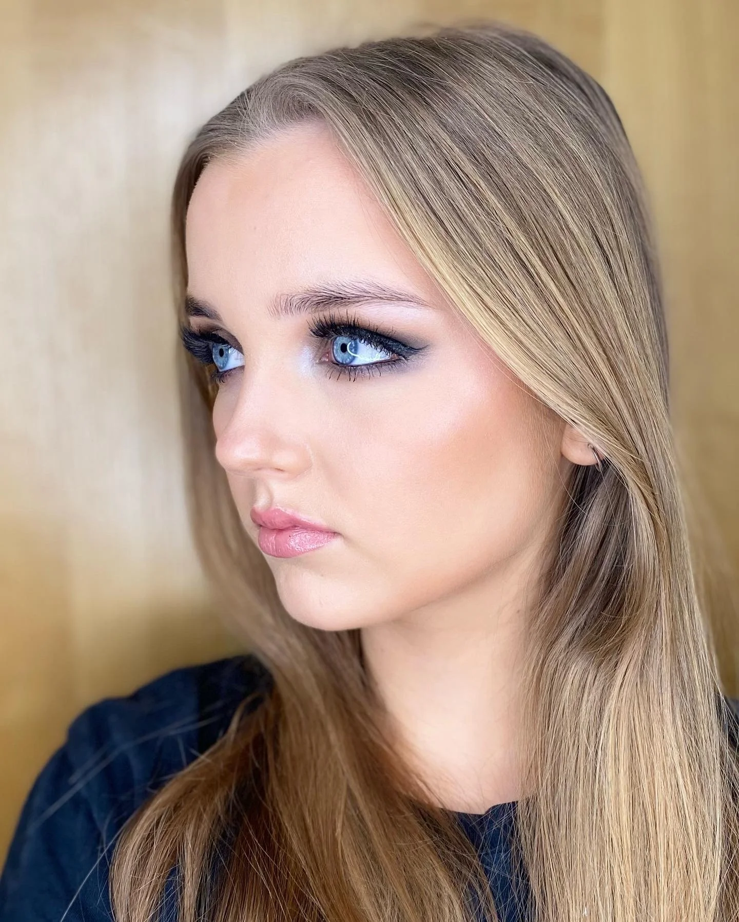 Close-up of a young woman with long, straight blonde hair looking to the side against a neutral background.