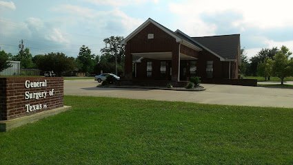 A brick building with a large parking lot in front and a sign that says 'General Surgery of Texas' near the entrance.