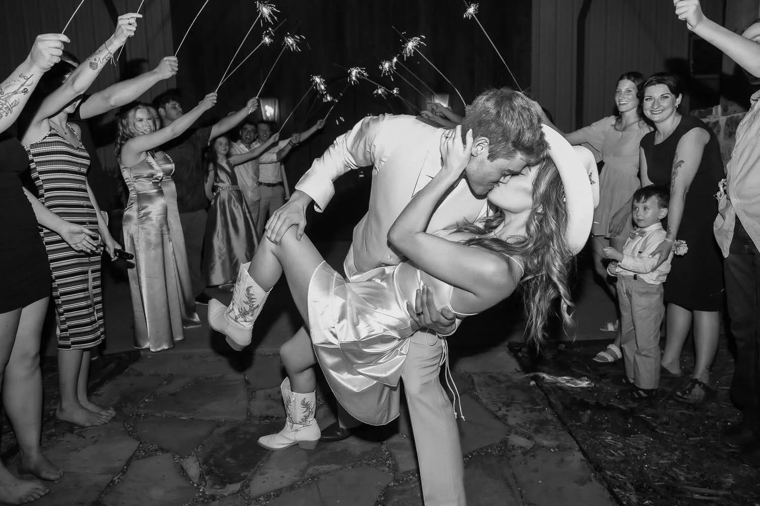 A couple is dancing closely at a celebration, surrounded by guests holding sparklers and watching them, at night or indoors.