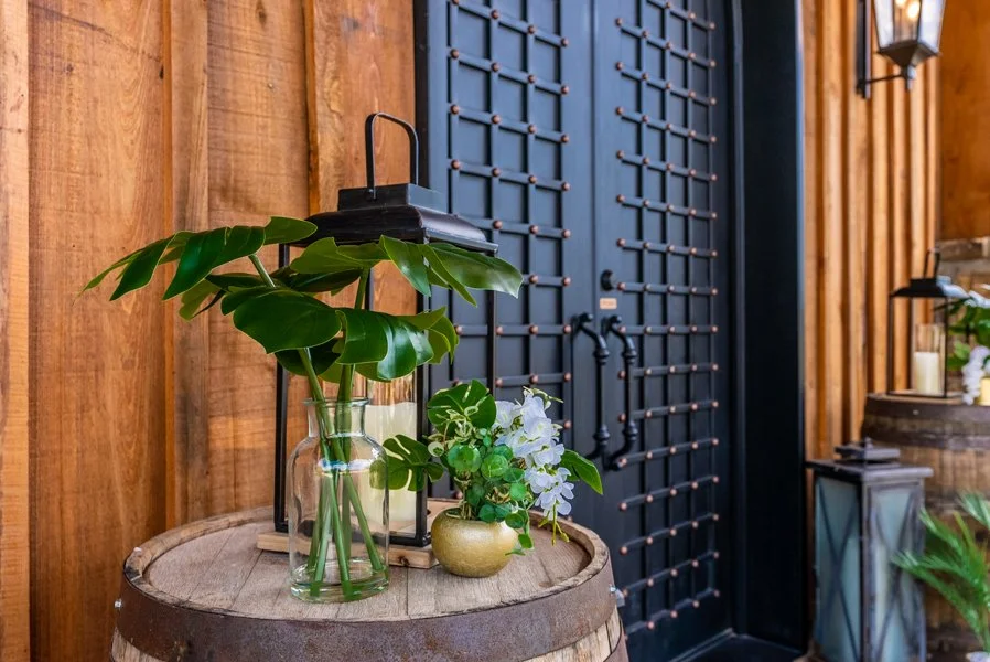 Decorative interior scene with potted plants, lantern, and black door with copper accents in a wooden room.