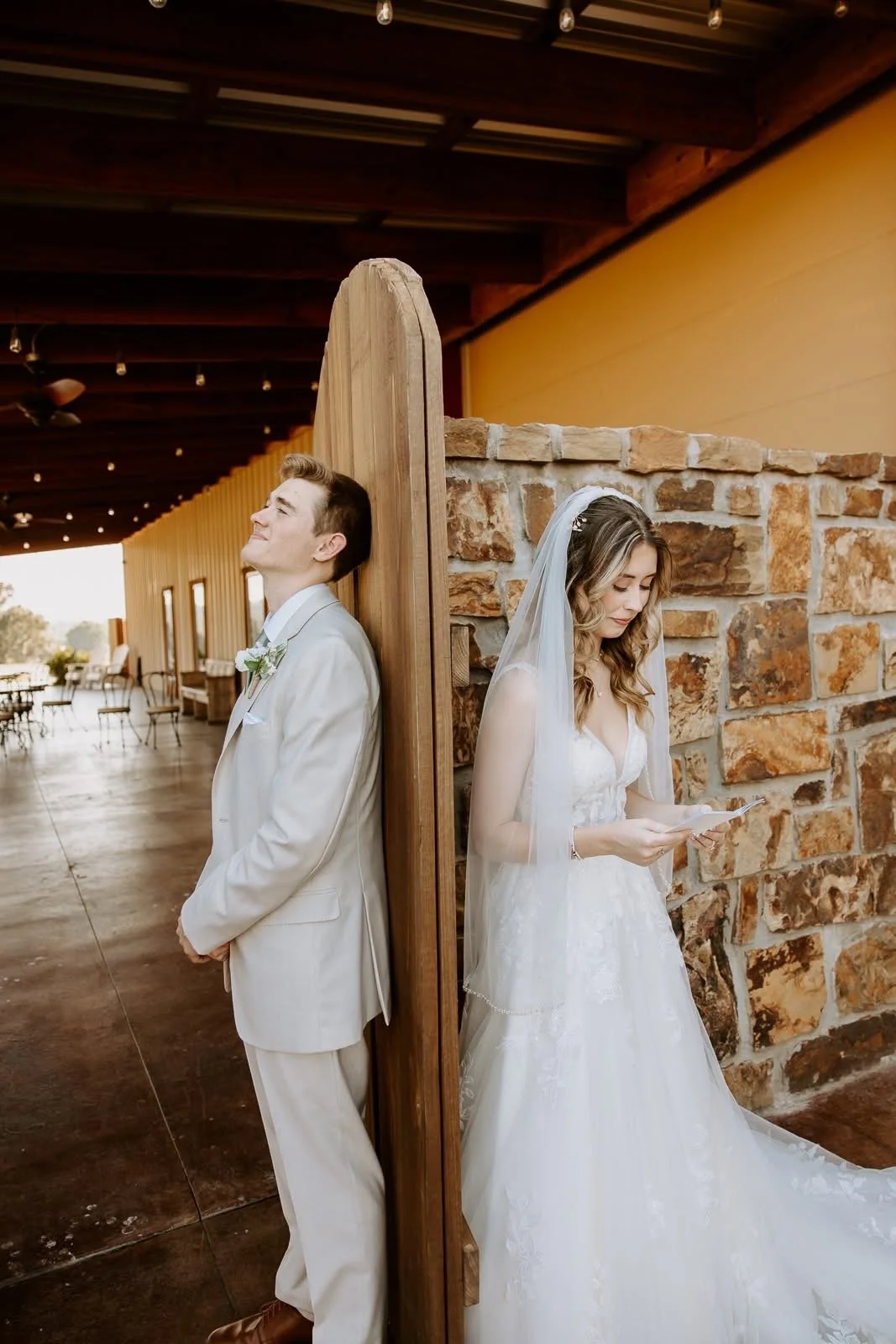 Bride and groom standing back-to-back separated by a wooden partition, indoors with rustic decor.