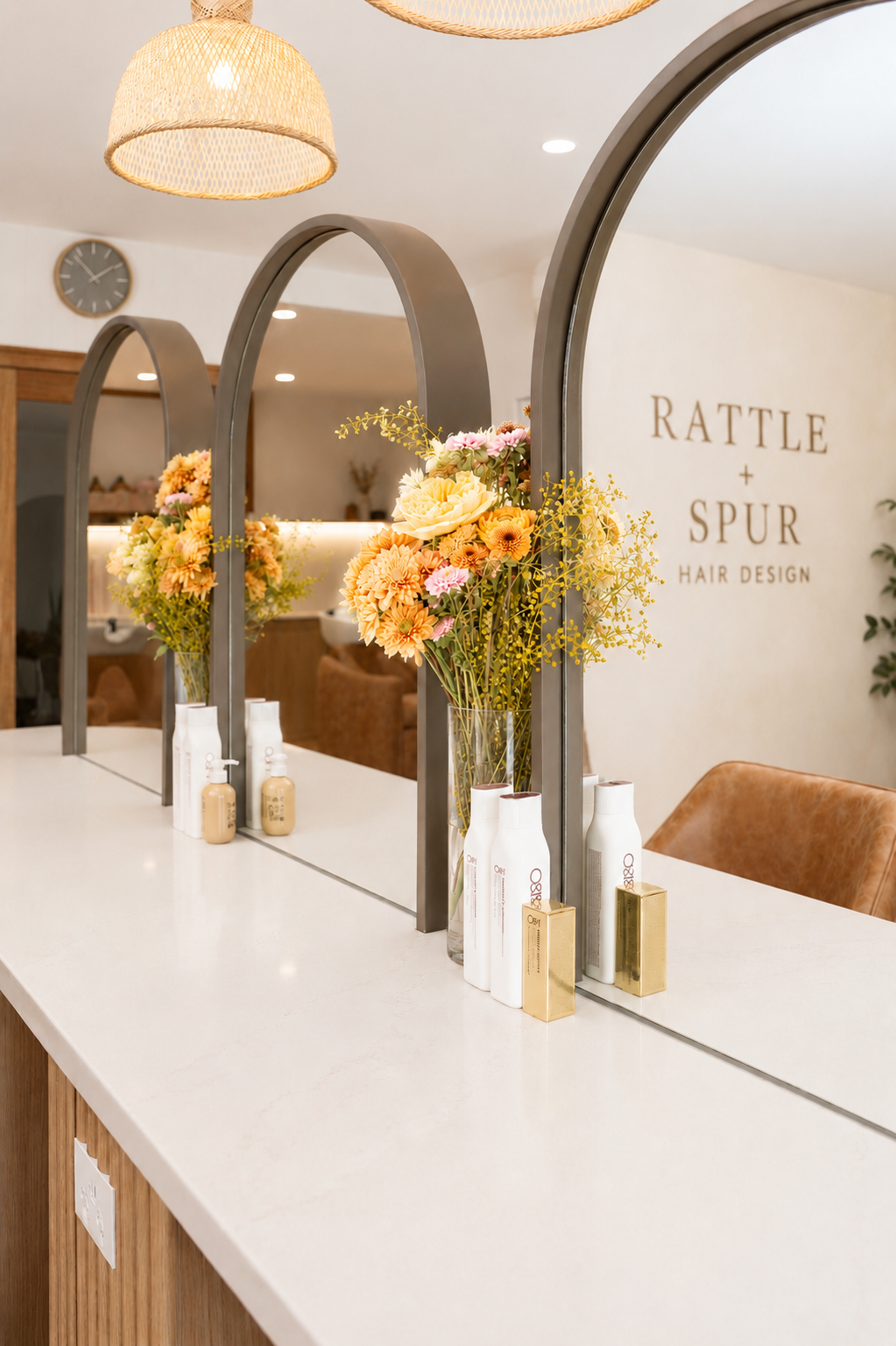 Reception desk with two large mirrors, floral arrangements, and hair products at Rattle + Spur Hair Design salon.