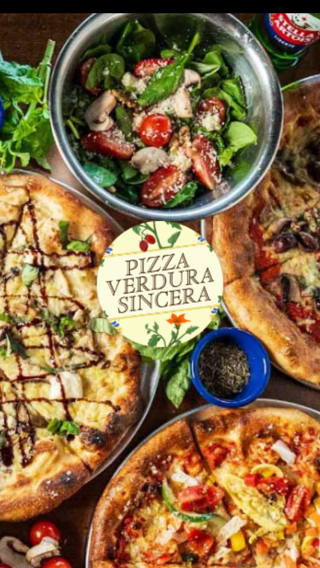 Assorted pizzas and a salad with cherry tomatoes, spinach, and grilled chicken in a bowl, with a sign that reads 'Pizza Verdura Sincera'.