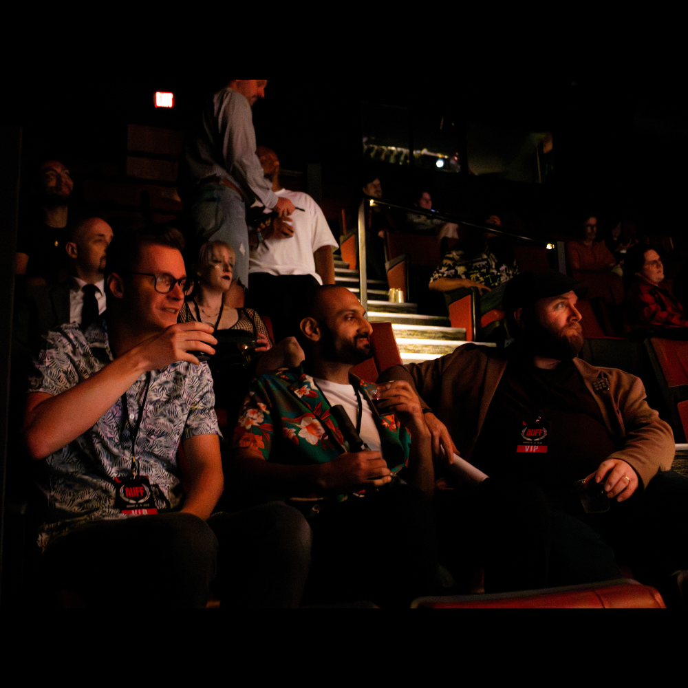 Audience seated in a theater, watching a performance or event, with some people holding drinks.