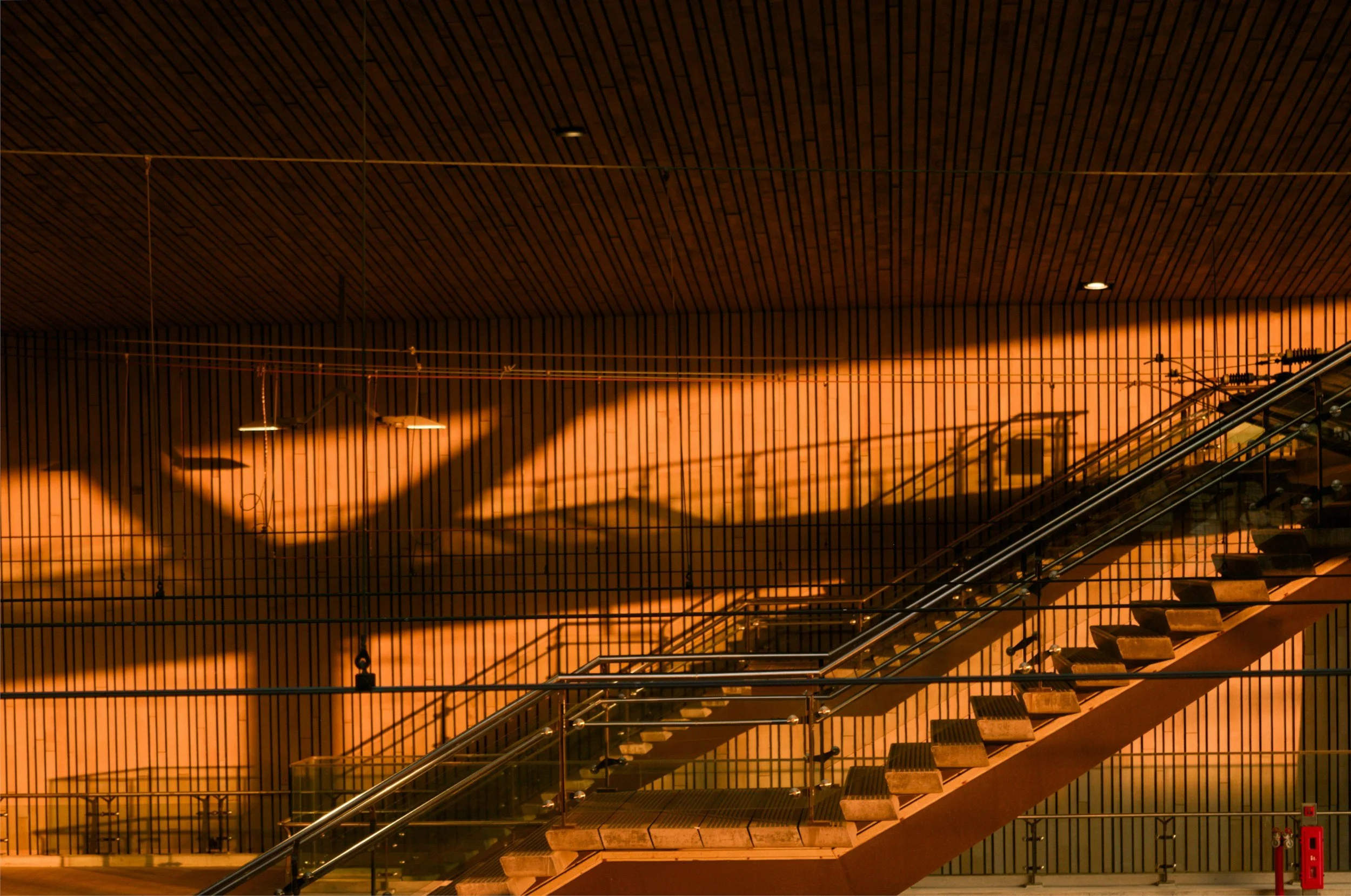 Interior of a modern building with wooden ceiling and staircase showing shadows and warm lighting.