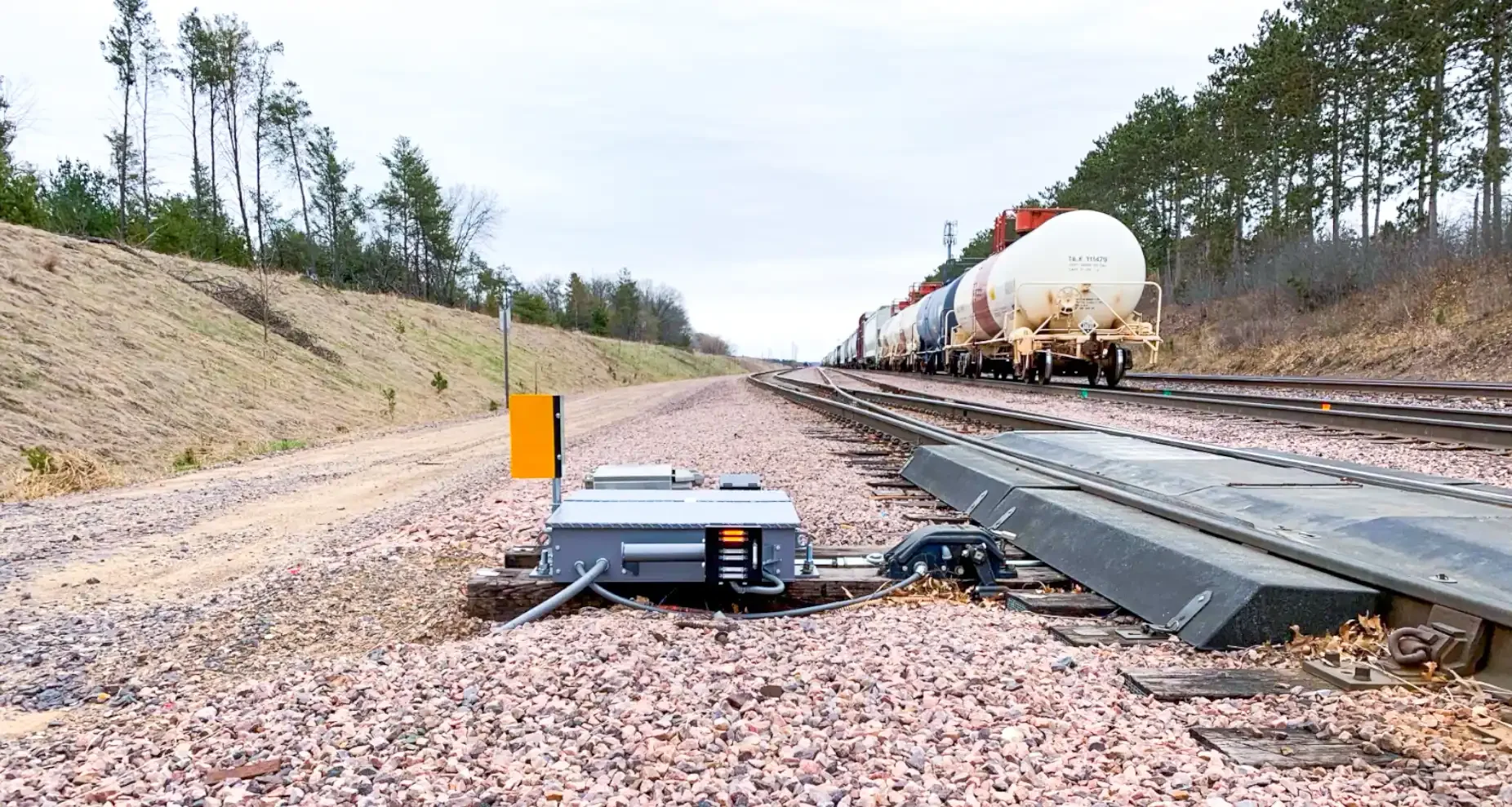 Railroad train with tanker cars passing through a rural area, viewed from a railway maintenance vehicle on the tracks.