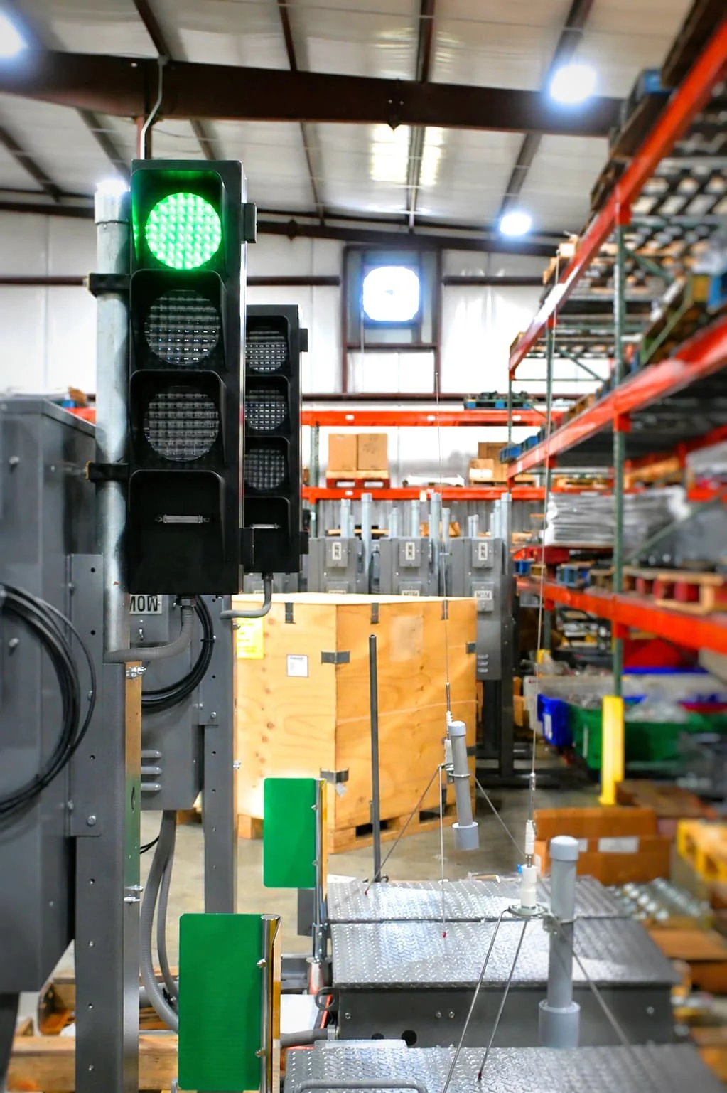 A green traffic light is turned on in an industrial warehouse, with shelves filled with boxes and equipment in the background.