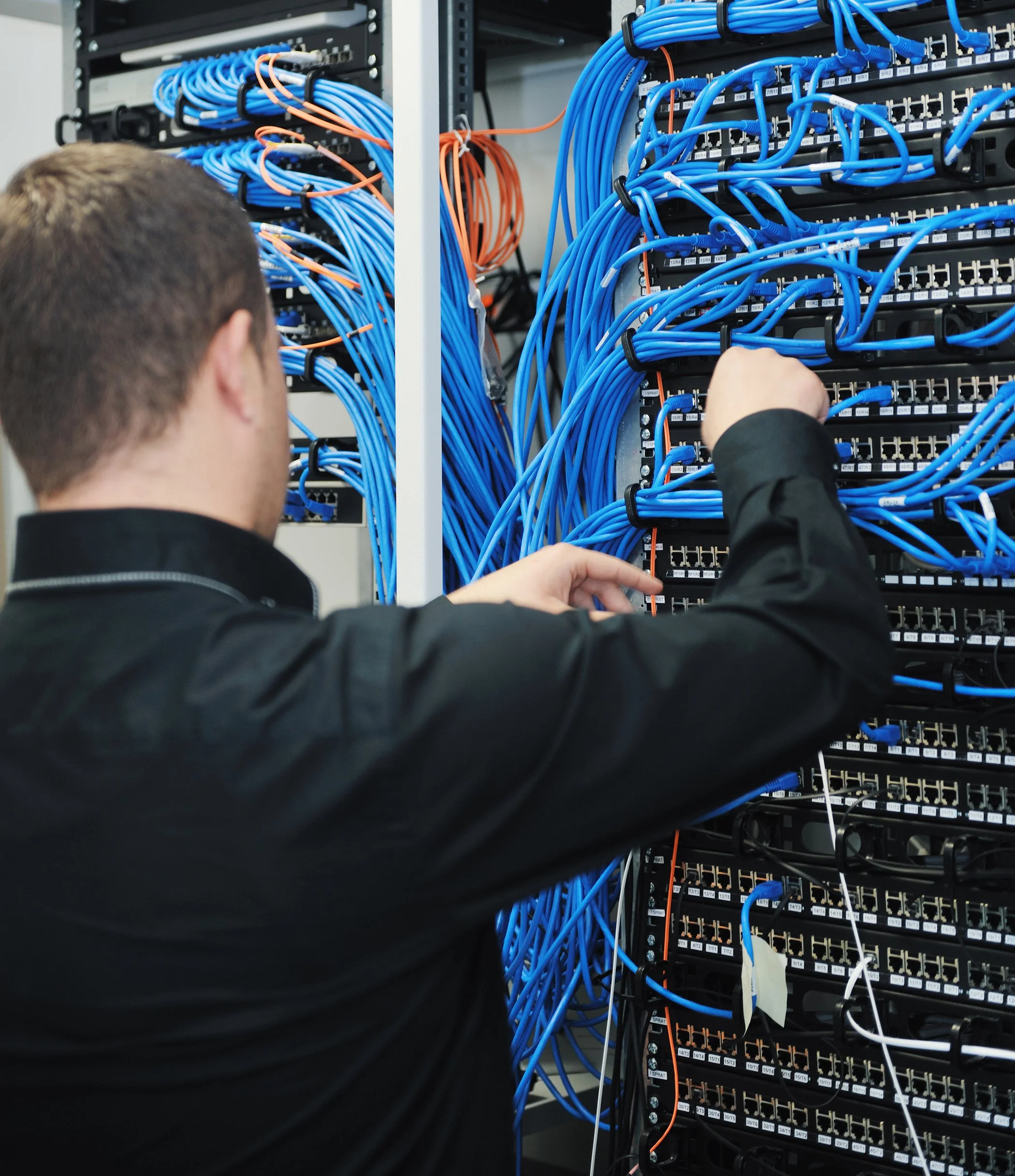 Close-up of a person working on a network server rack with numerous blue Ethernet cables connected to patch panels.