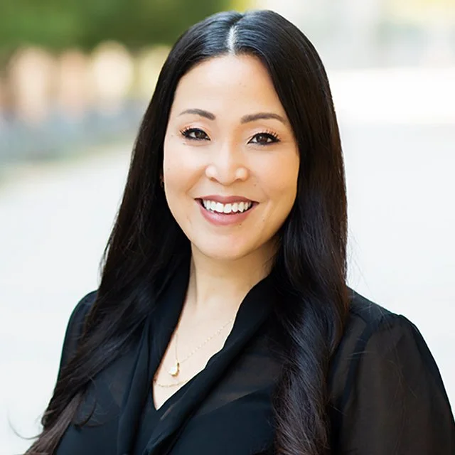 A smiling woman with long black hair wearing a black top outdoors.