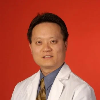 Portrait of a man wearing a white coat and a striped tie against a red background.
