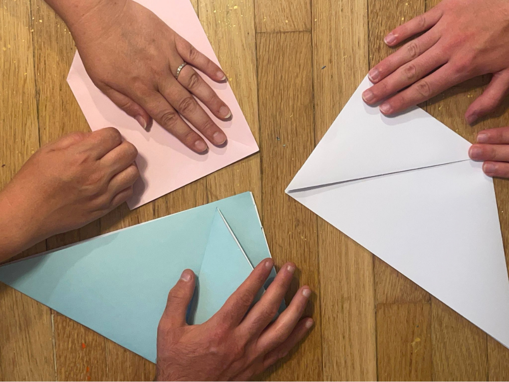 Photo of several different pairs of hands folding paper to make something origami