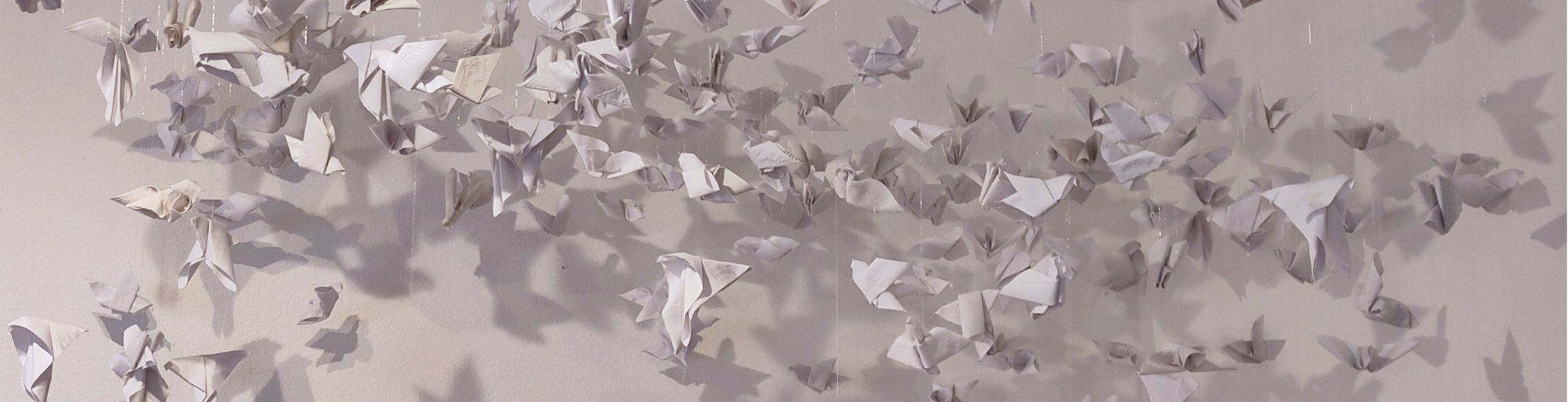 Photo of a flock of white origami birds made from cotton shirts suspended in the air
