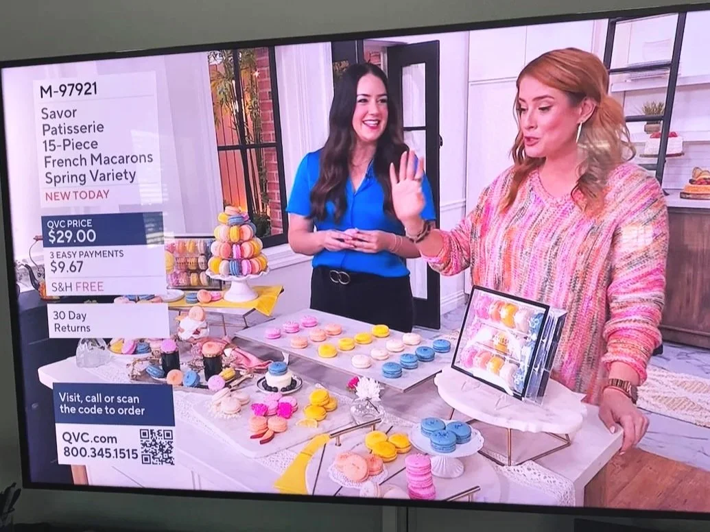 QVC presentation of Savor Patisserie 15-piece French macarons spring variety, with two hosts and colorful macarons displayed on tables.