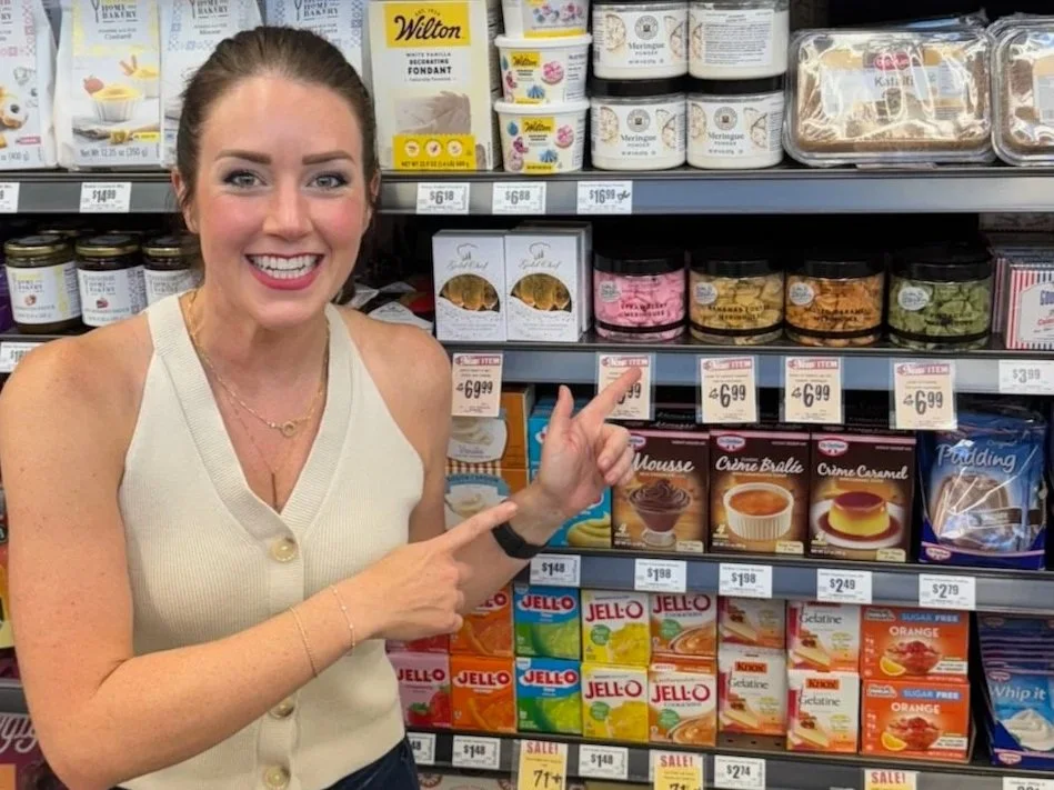 Smiling woman pointing to dessert mixes and baking supplies on a grocery store shelf