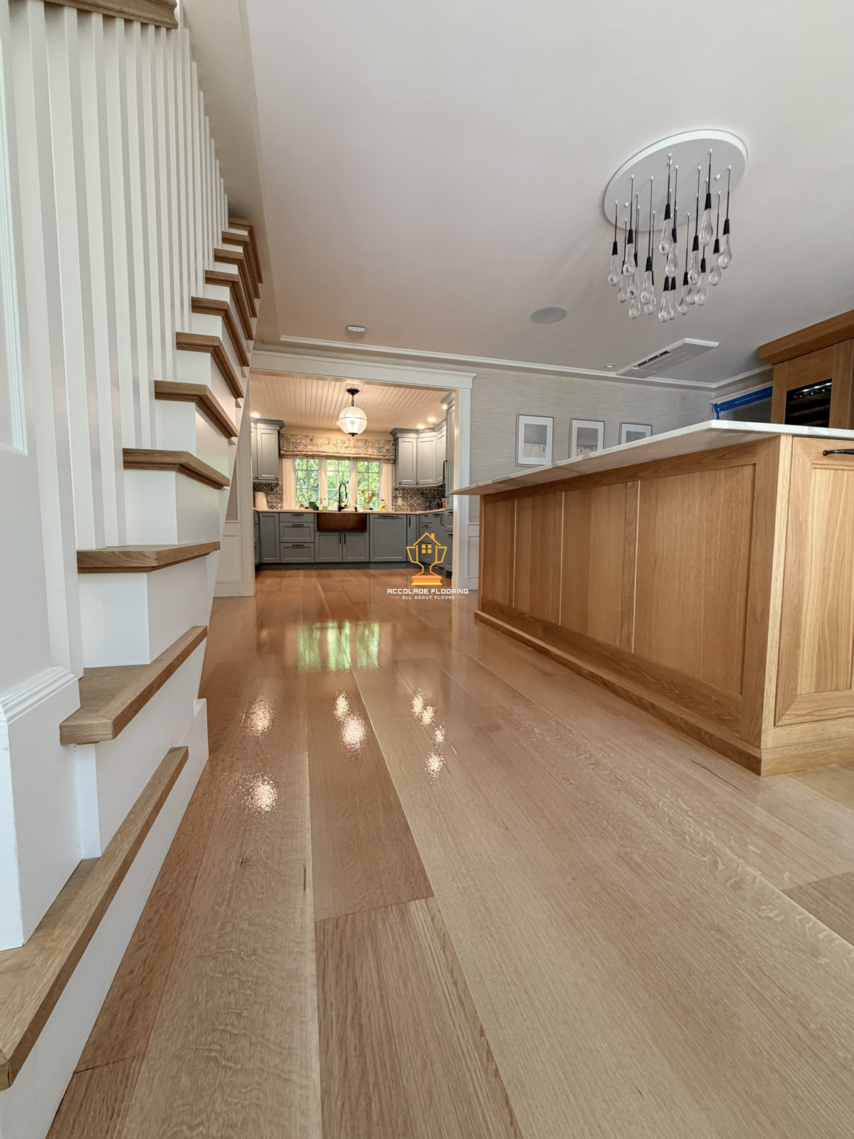 Open living space with light wood flooring, a kitchen with gray cabinets, a white ceiling, and decorative light fixtures.