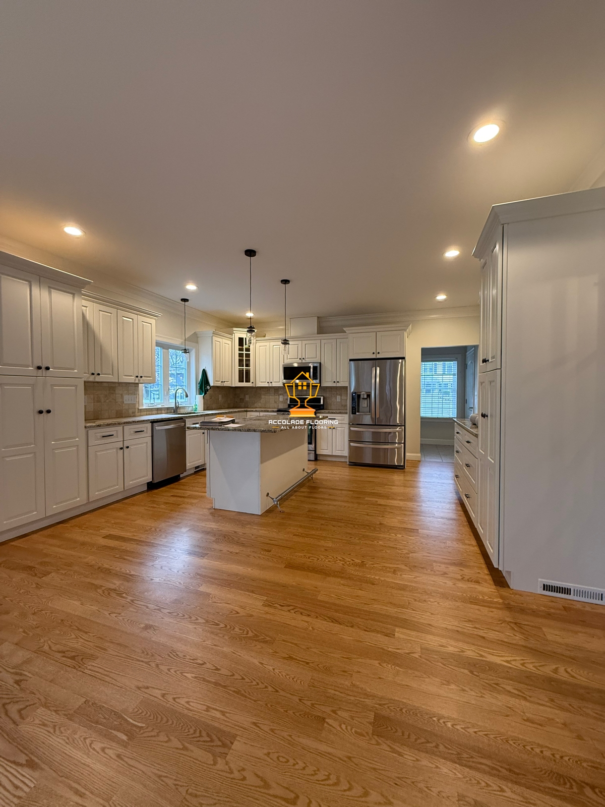 A spacious kitchen with white cabinetry, hardwood flooring, stainless steel appliances, and a central island with pendant lighting.
