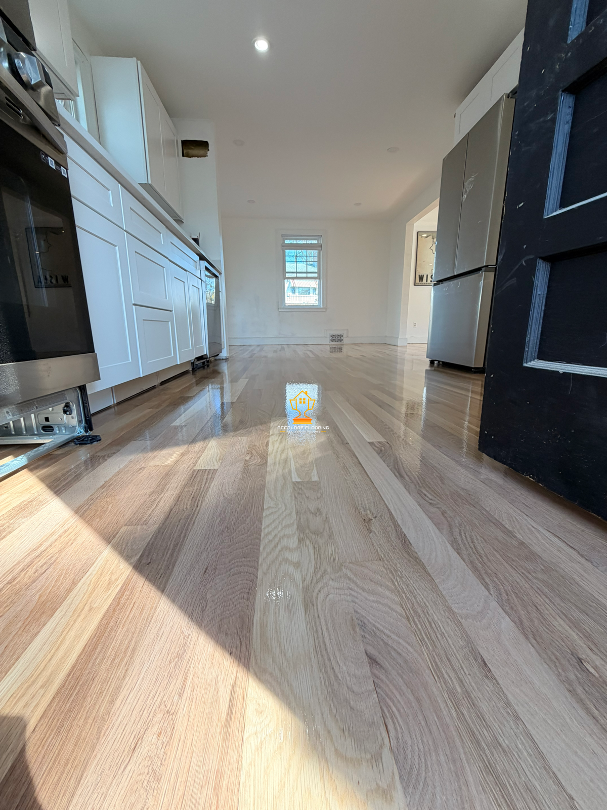 Photo of a kitchen with light-colored hardwood floors, white cabinets, and stainless steel appliances, taken from a low angle near the floor.